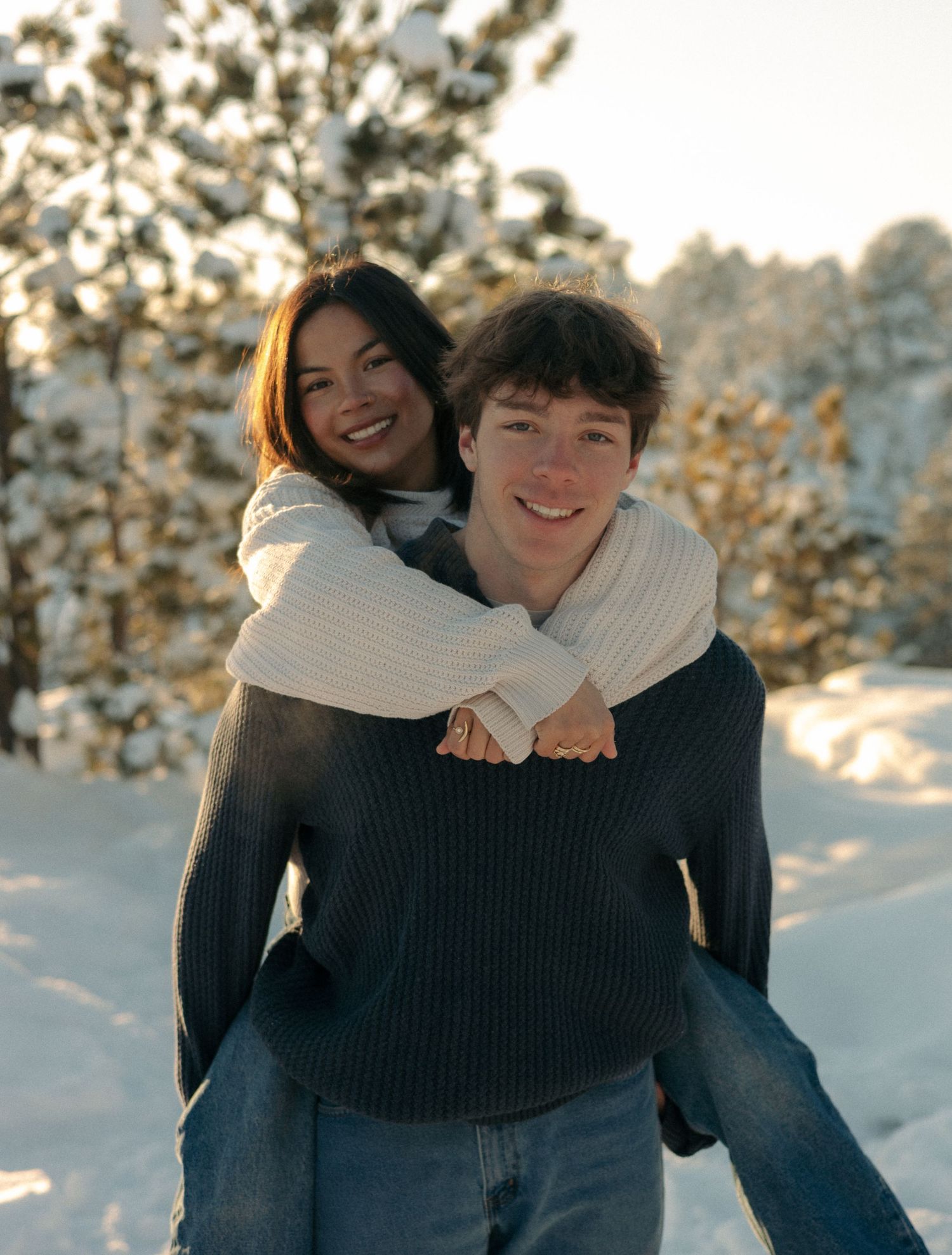 Smiling woman riding piggyback on mans back in snowy winter forest setting.