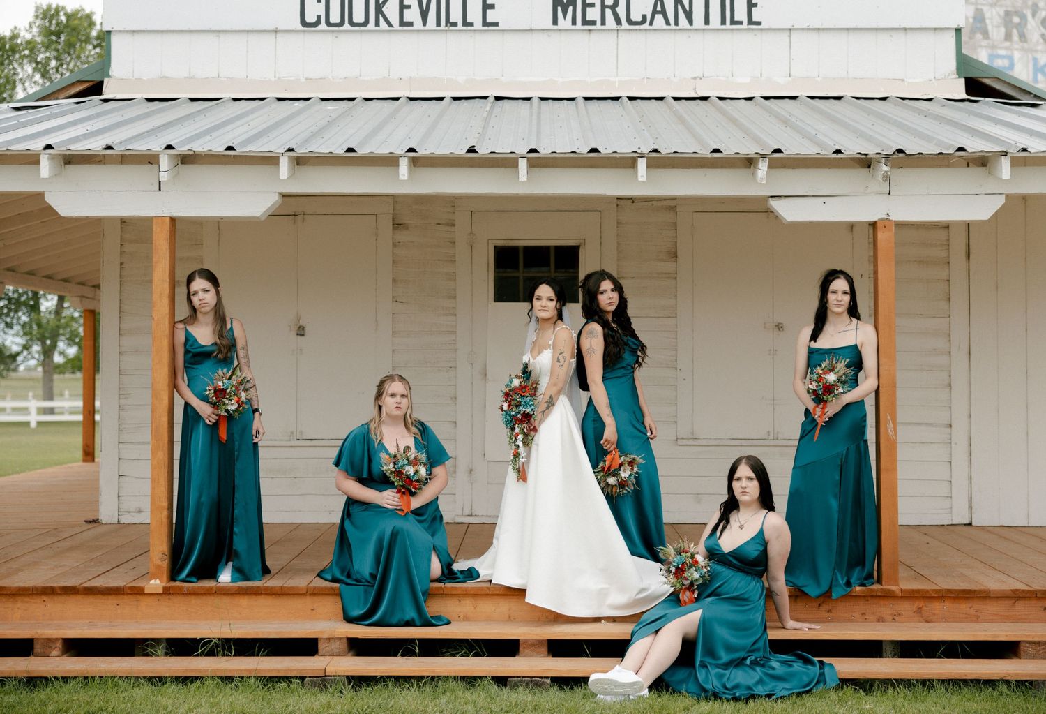 Bride in white gown with bridesmaids in teal dresses on porch of Cookeville Mercantile holding bouquets.