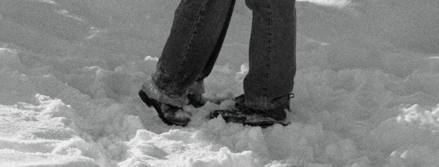 Close-up black and white photo of two people standing together in deep snow wearing jeans and boots.