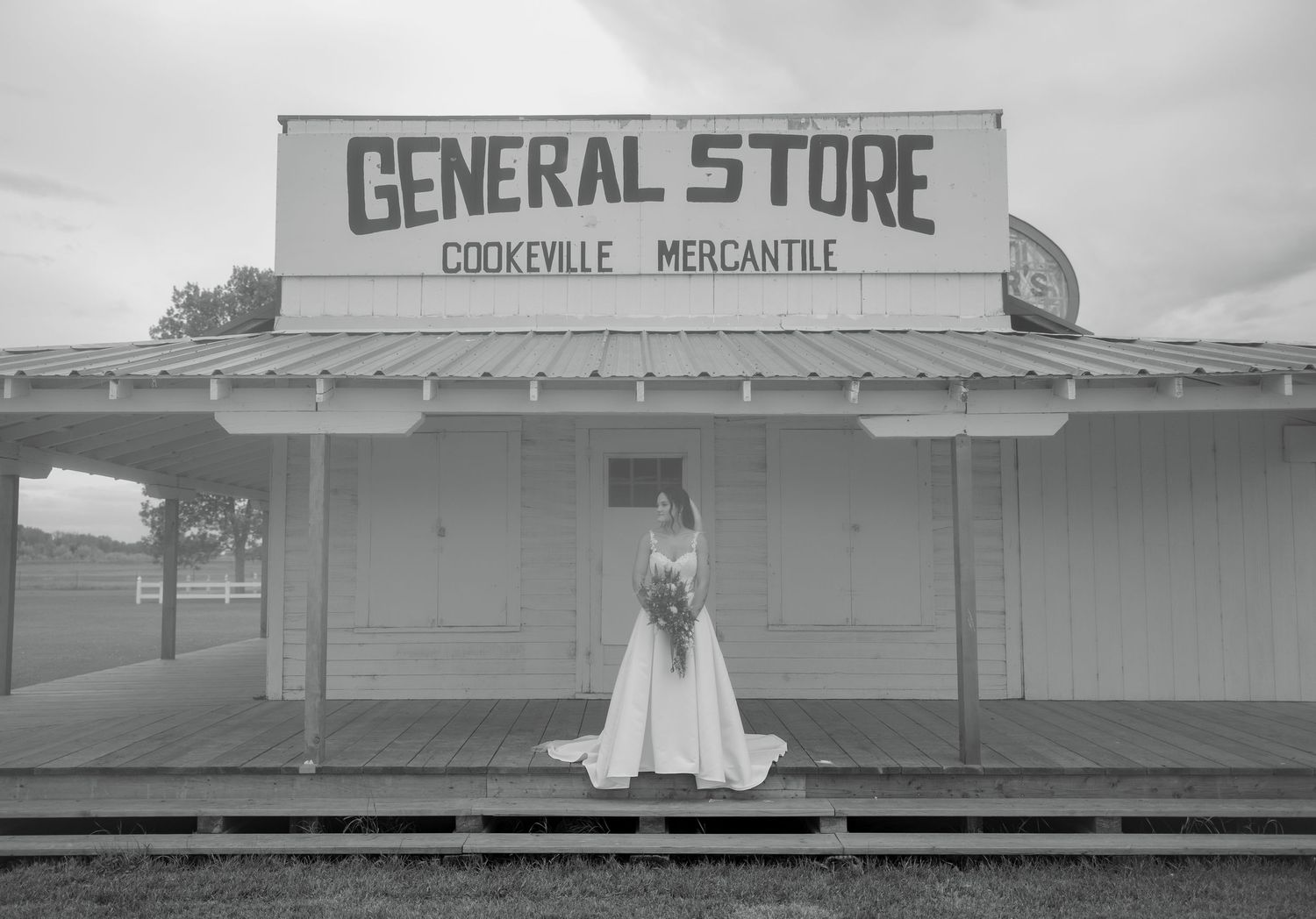 Bride in white gown poses before a rustic General Store Cookeville Mercantile building in a black and white photo.