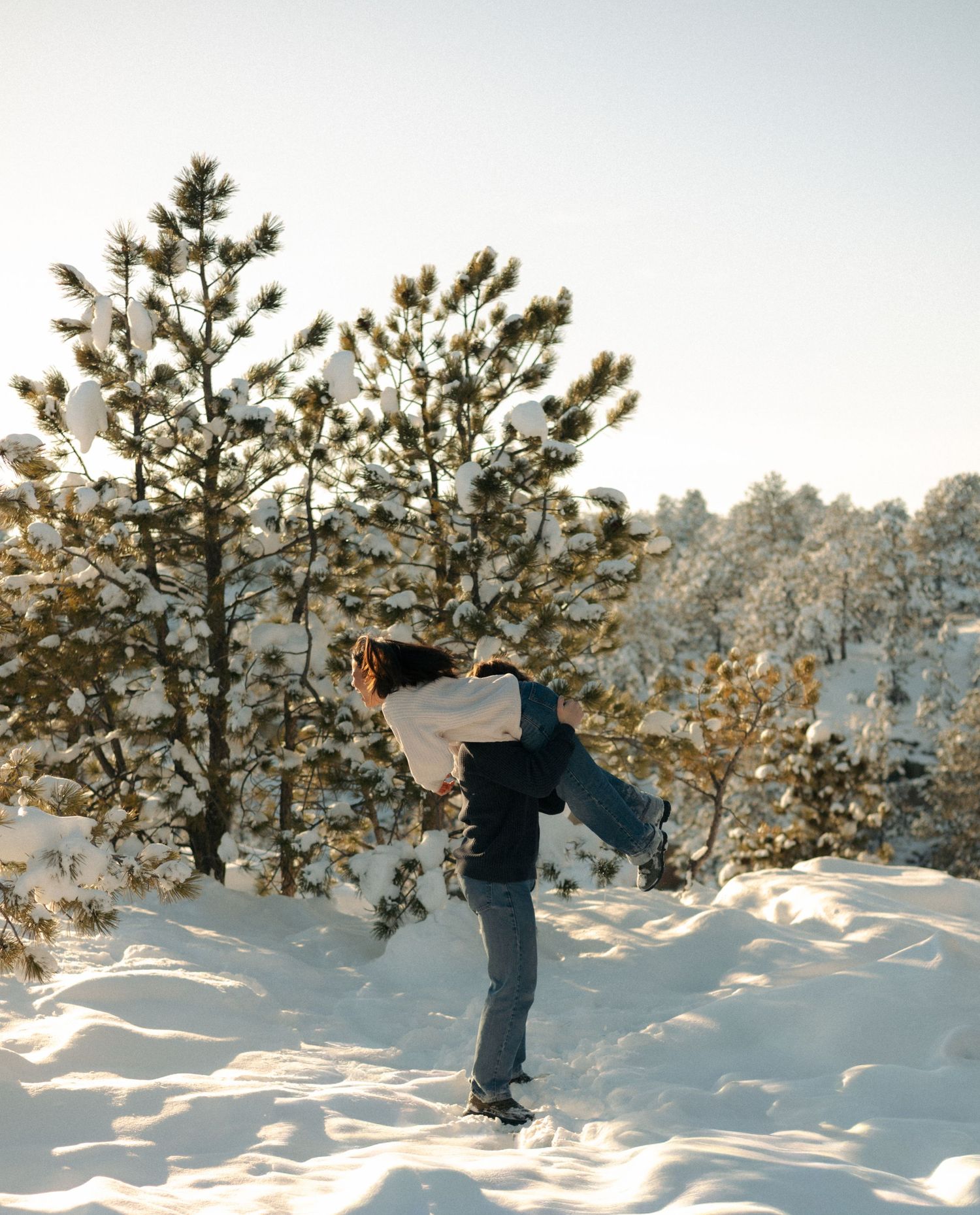 Person giving piggyback ride in snowy winter forest with snow-dusted pine trees.