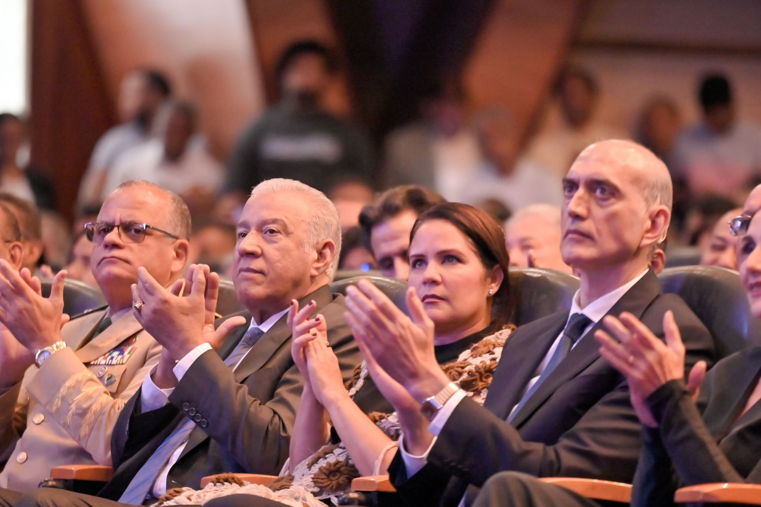 Audience members in formal attire applauding at an indoor academic or corporate event.