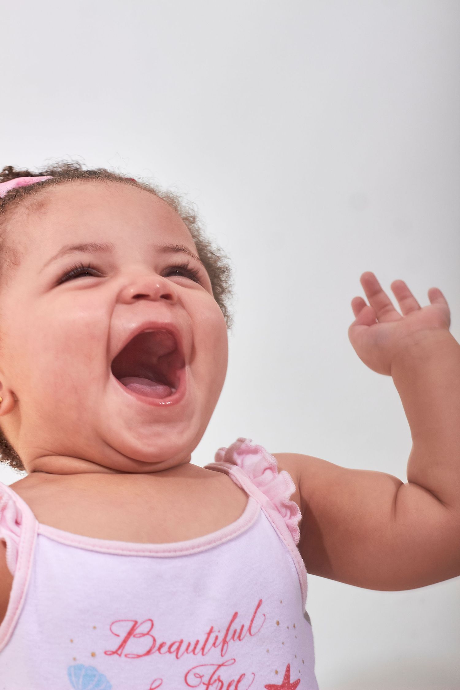 Happy laughing baby girl in pink Beautiful top reaching hand up against white background.