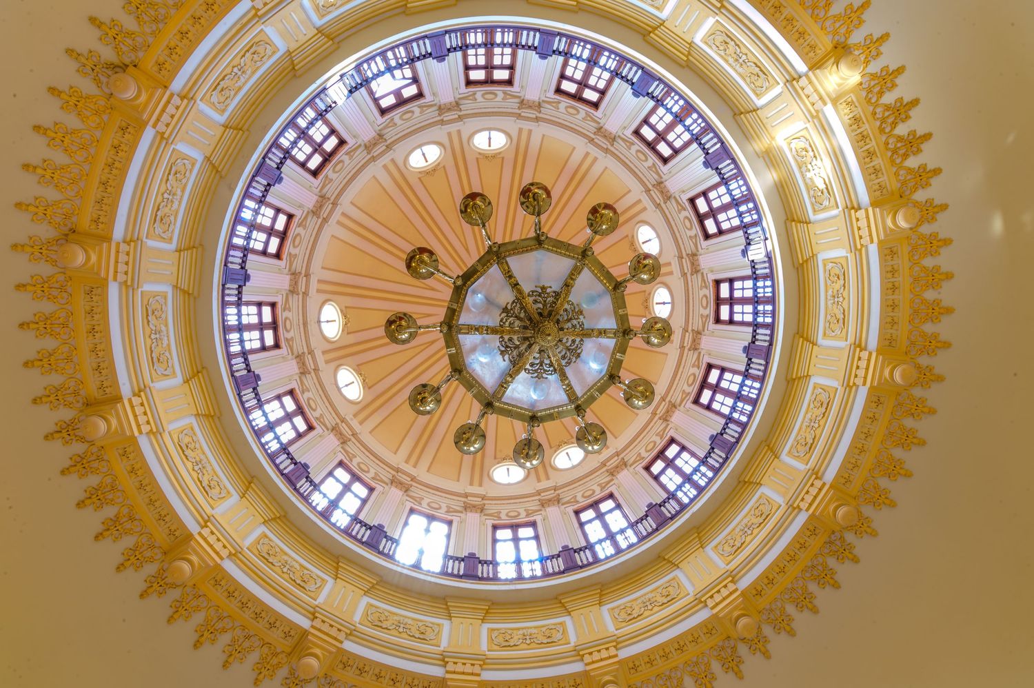 Looking up at an ornate domed ceiling with stained glass, chandelier, and intricate gold decorative details.