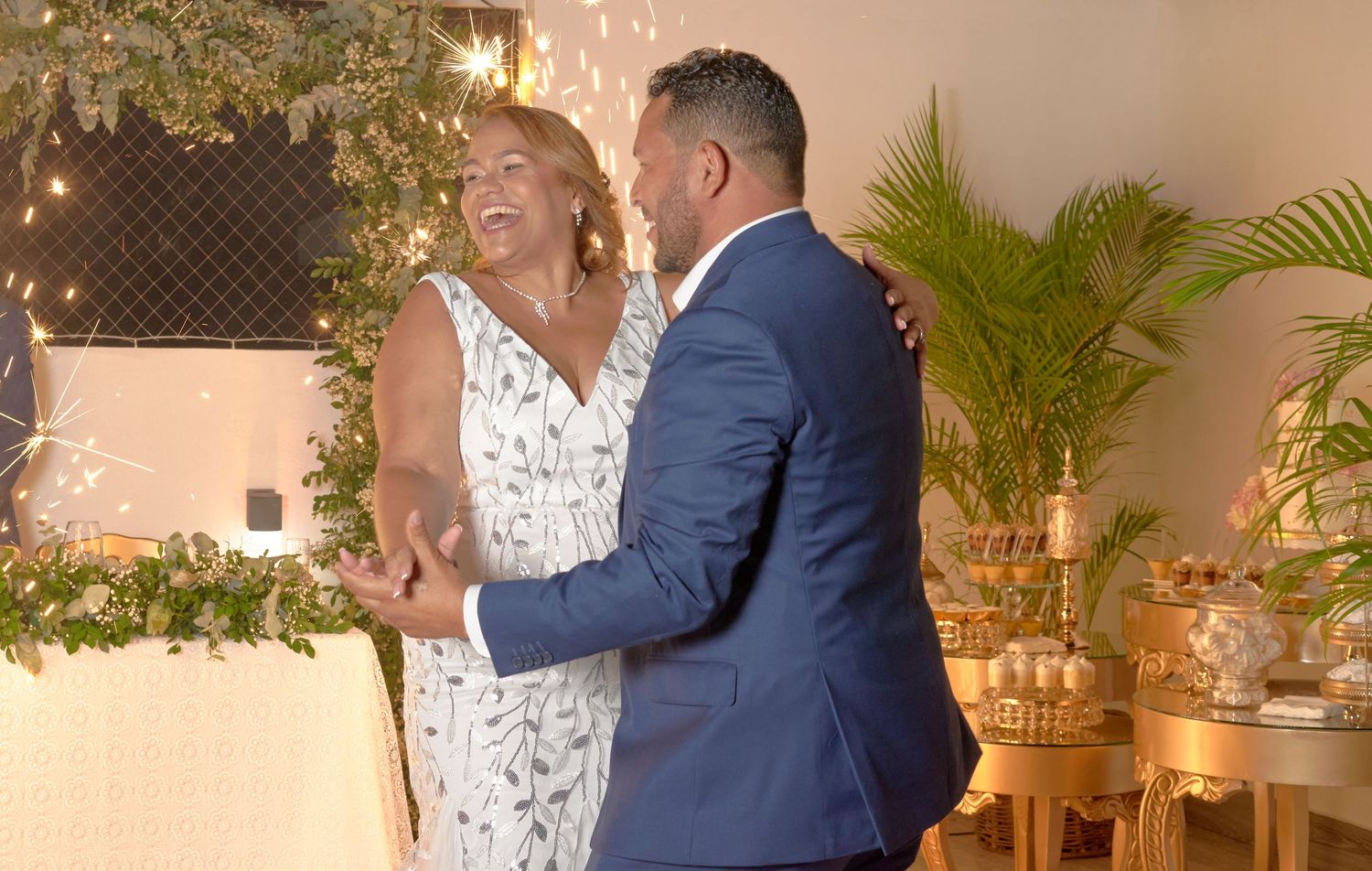 Happy bride and groom sharing first dance surrounded by greenery at wedding reception.