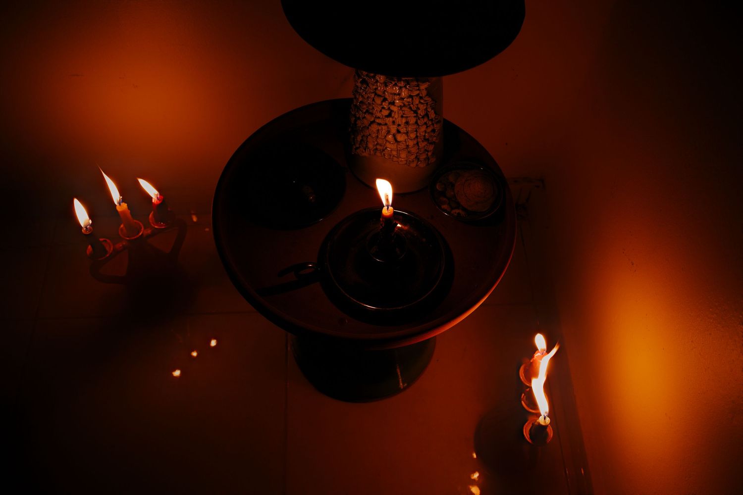 Ornate chandelier with lit candles glowing in warm amber light against a dark background.