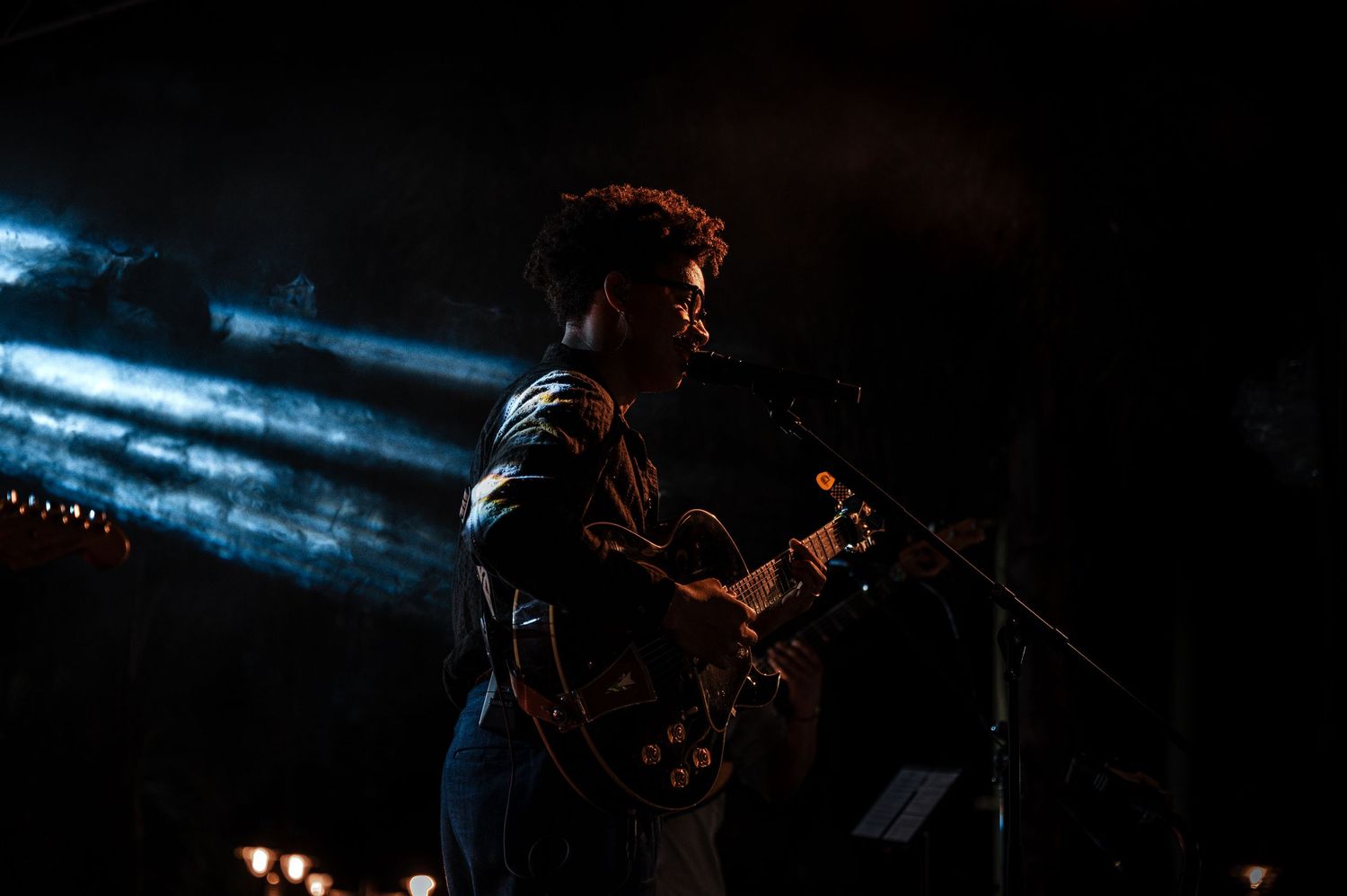 A guitarist performing on stage under dramatic blue spotlights during a live concert in a dark venue.