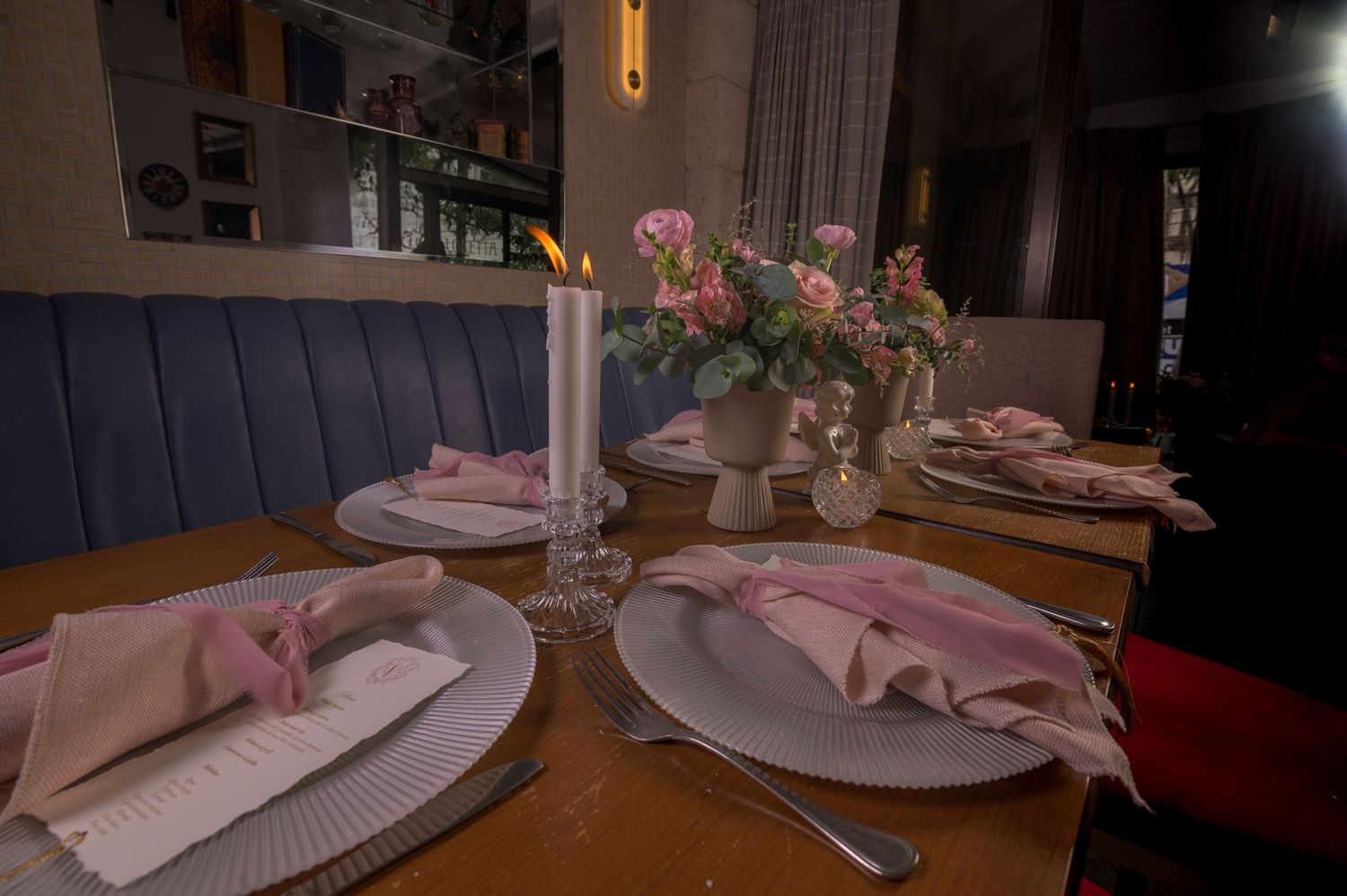 Romantic candlelit dinner table set with pink napkins and rose floral arrangement.