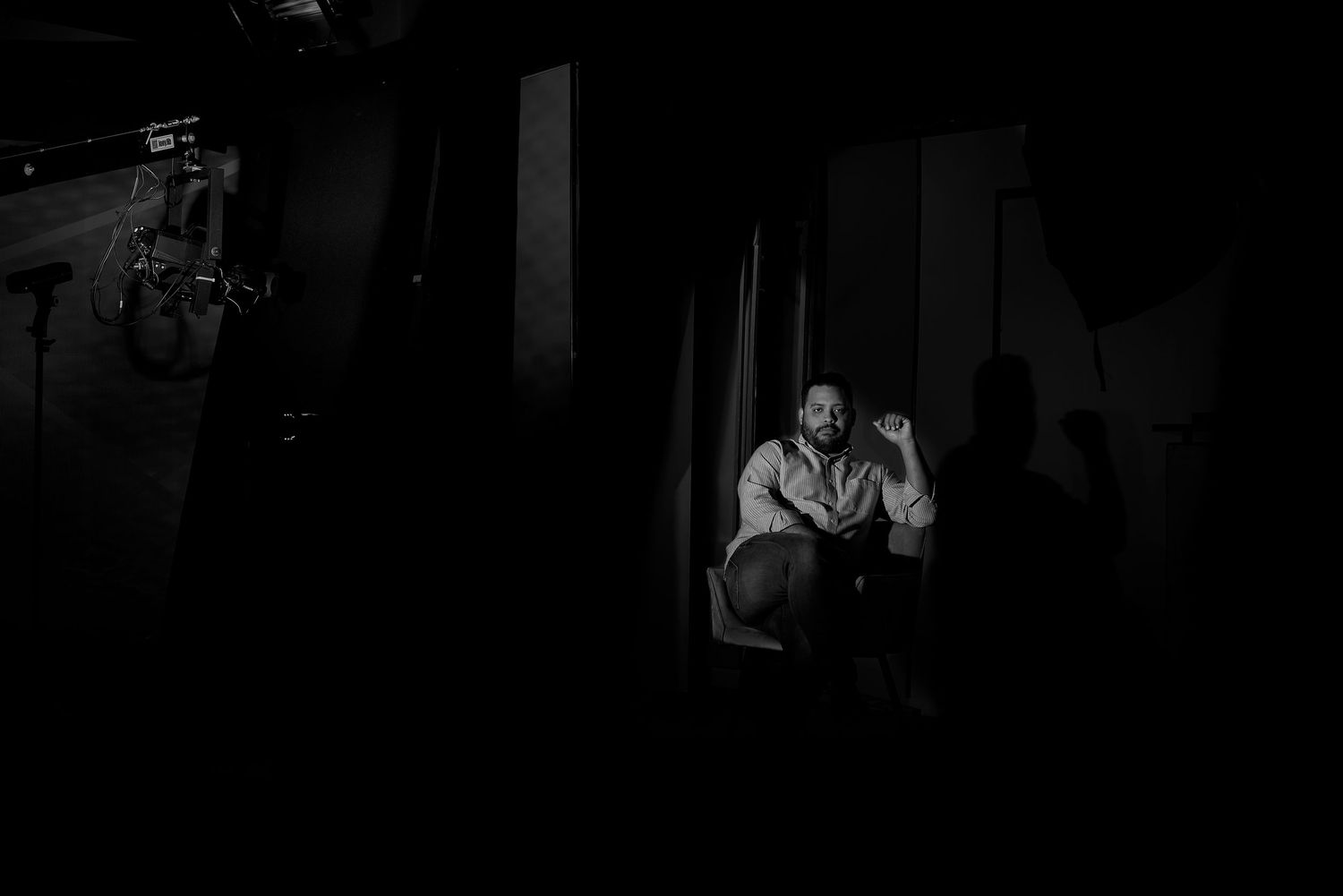 Black and white dramatic portrait of a man sitting alone in a dimly lit backstage area with shadows.