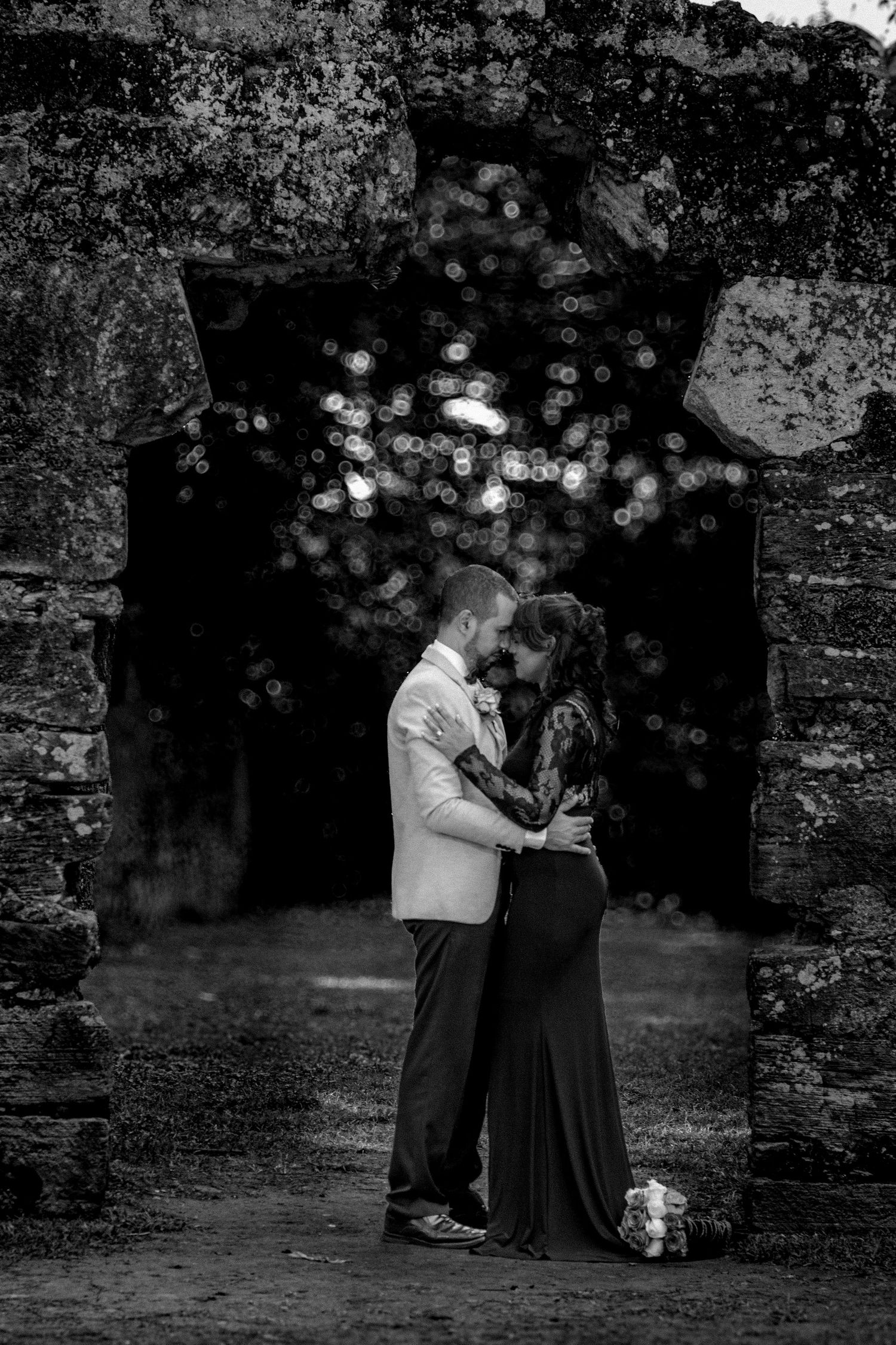 Black and white romantic couple kissing inside ancient stone archway ruins.