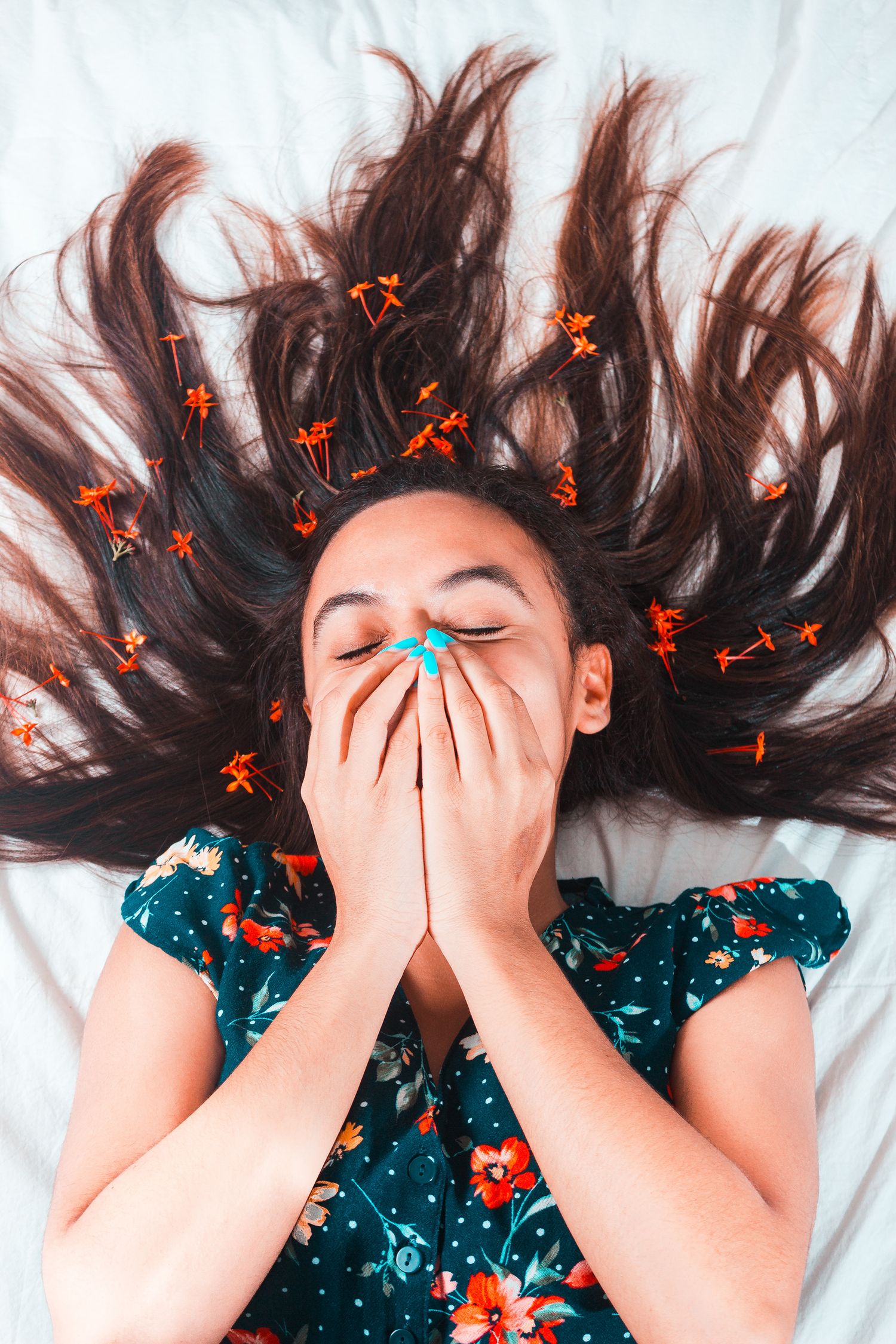 Young woman lying on white surface with flowers in her flowing dark hair.