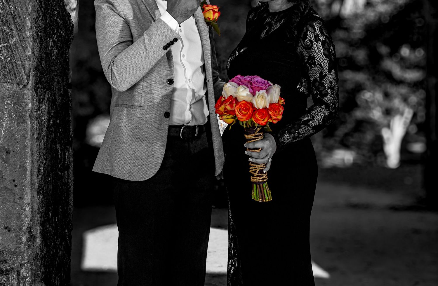 Black and white photo of couple holding vibrant orange and pink rose bouquet.