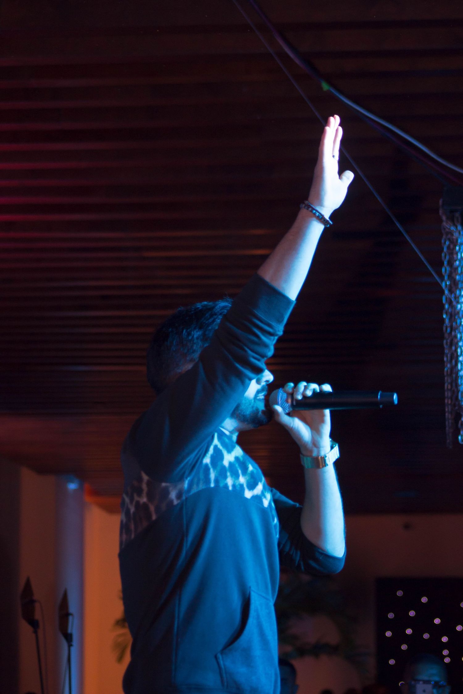Singer performing on stage with one hand raised holding a microphone under blue light.