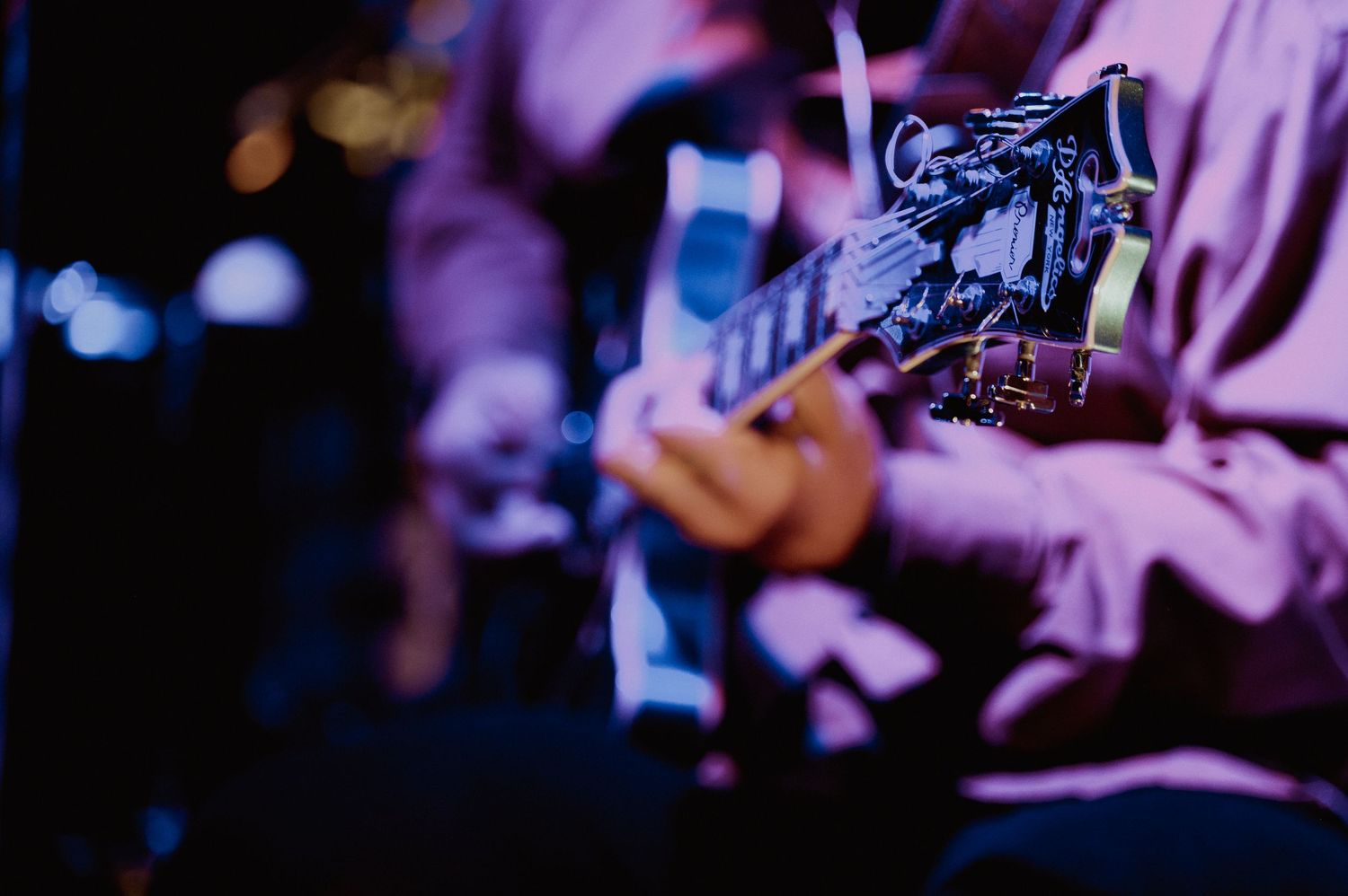 Close-up of musician playing electric guitar under blue and purple stage lighting at live concert.