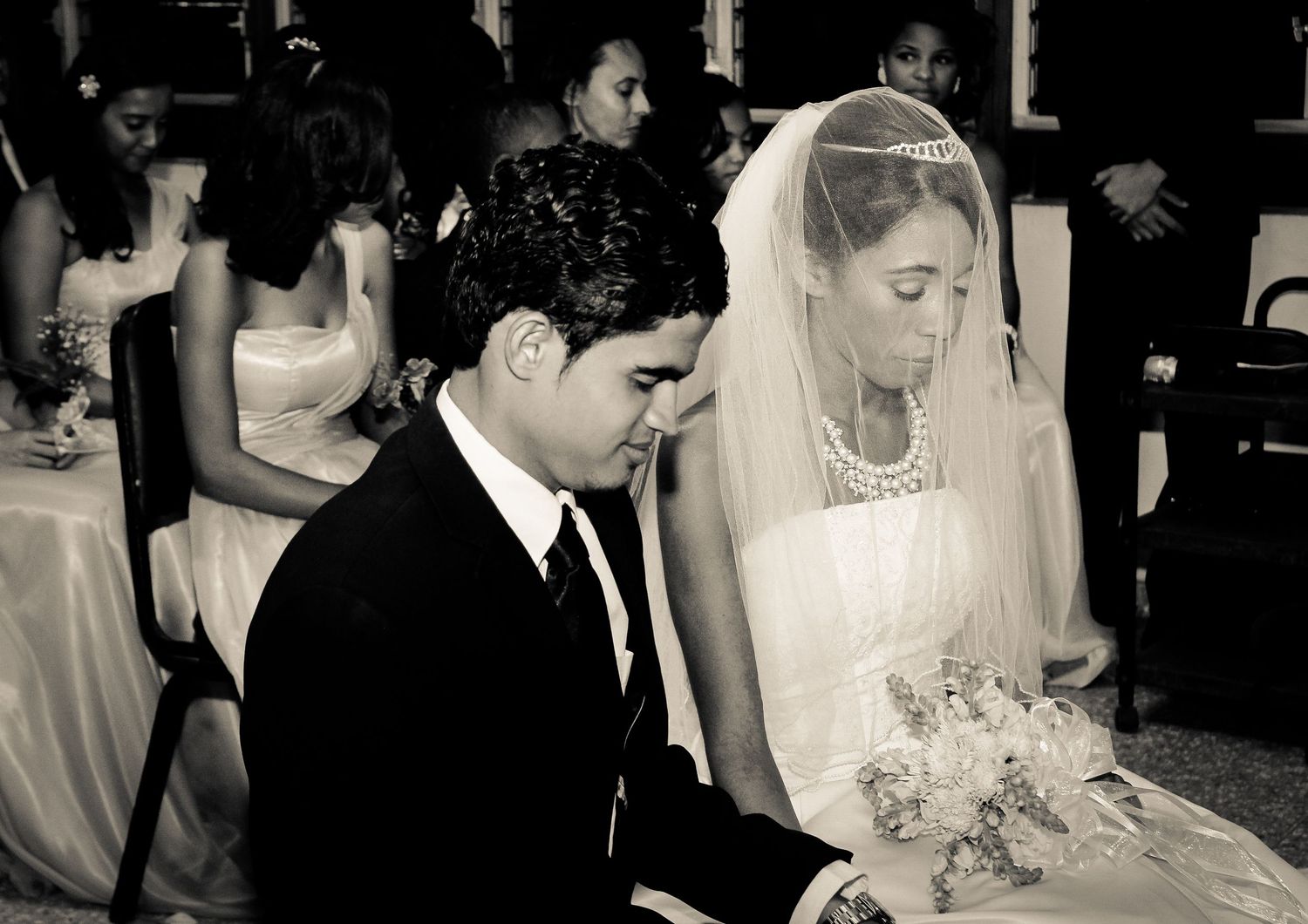 Black and white photo of bride and groom bowing heads in prayer during wedding ceremony.
