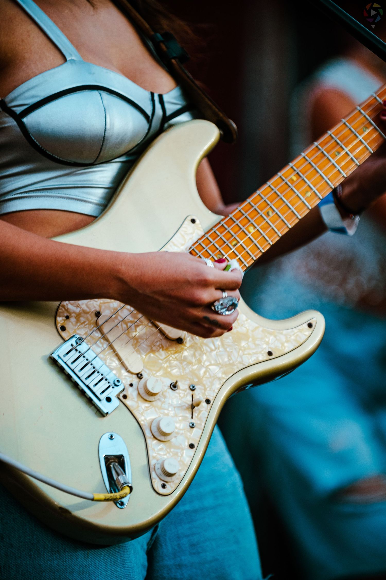 Woman playing cream Fender Stratocaster electric guitar wearing blue crop top.