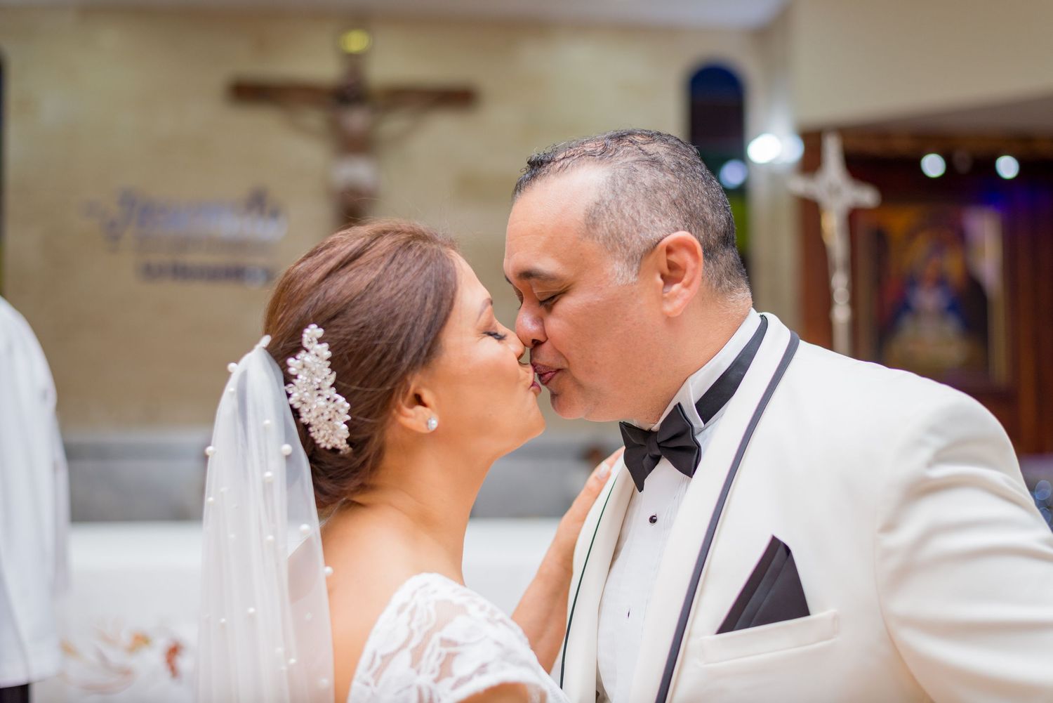 Bride and groom share first kiss at altar in Catholic church during wedding ceremony.