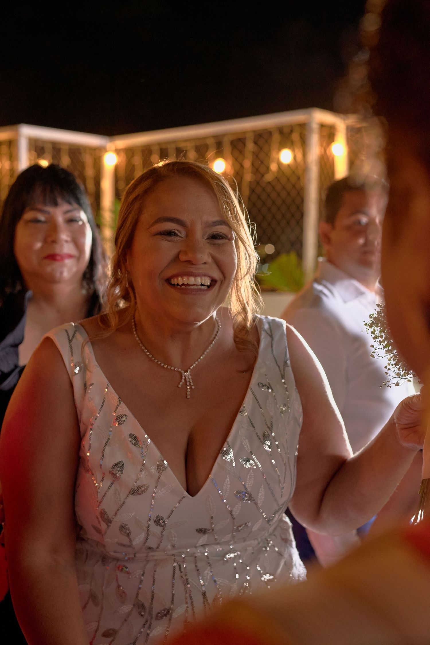 Radiant bride in sequined white gown laughing joyfully during wedding reception celebration.