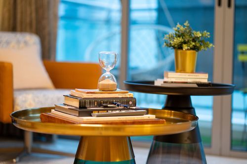 Stylish gold side table with stacked books and hourglass beside a plant on a dark round table.