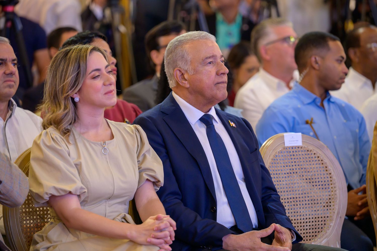 Older man in blue suit and young woman in gold dress seated together at formal event.