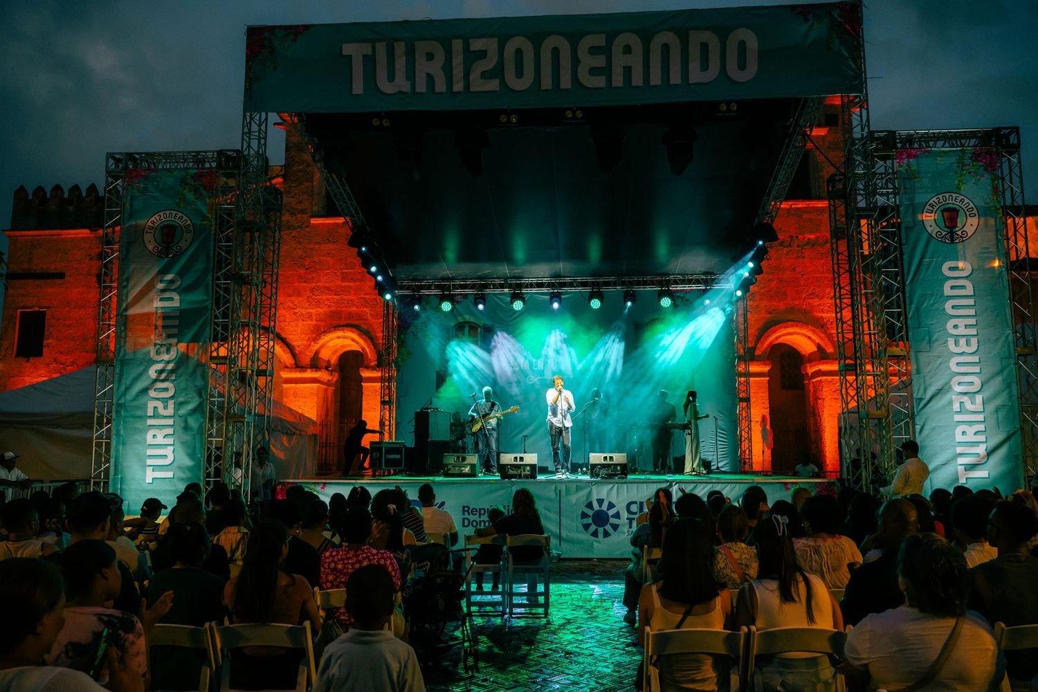 Turizoneando music festival stage with performers and colorful lights at an outdoor evening concert.