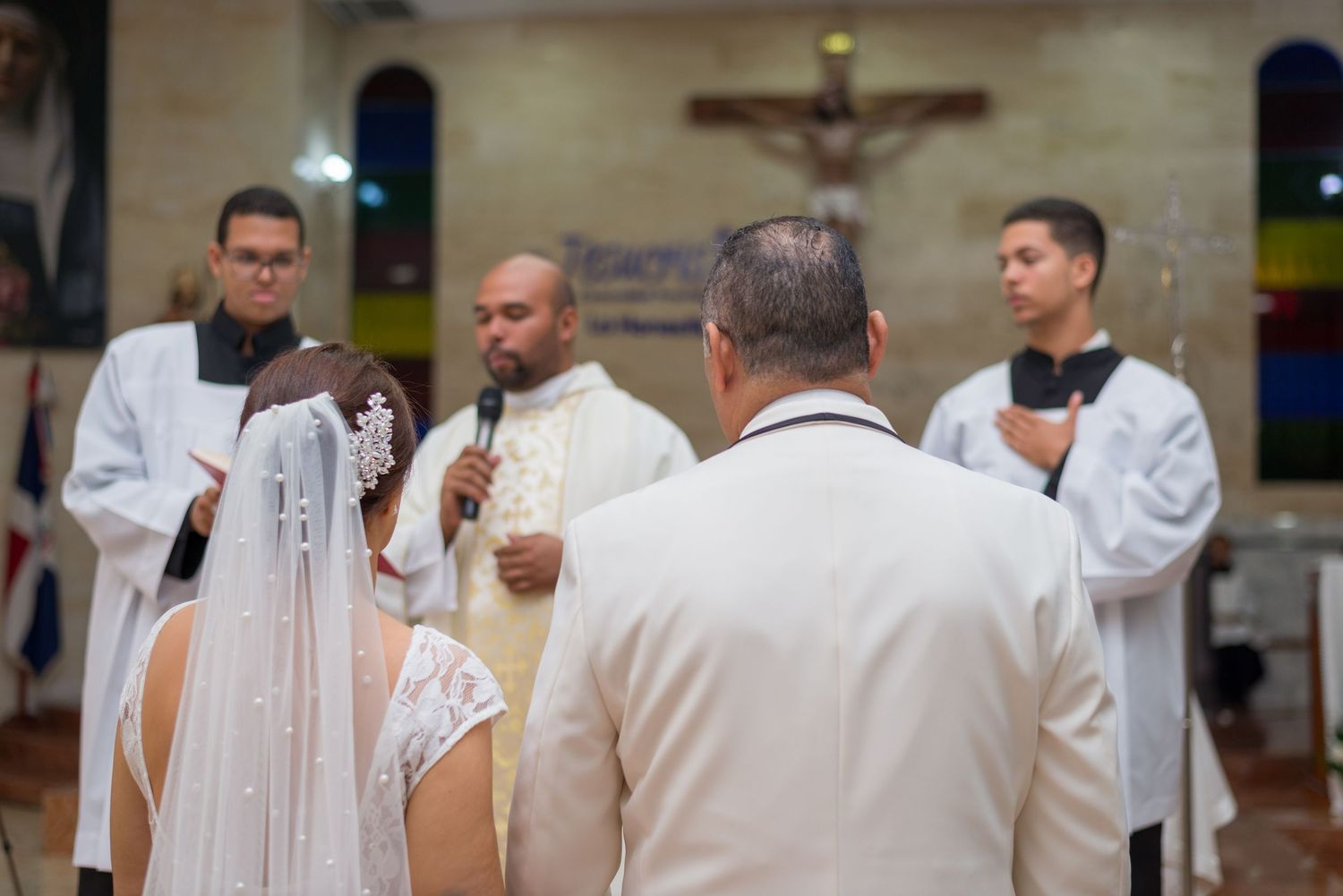 Bride and groom stand before priest and altar servers during Catholic wedding ceremony.