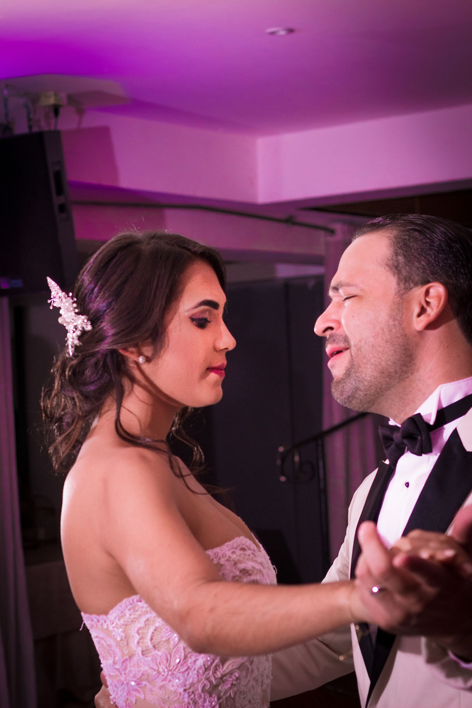 Bride and groom sharing intimate first dance moment at wedding reception under purple ambient lighting.