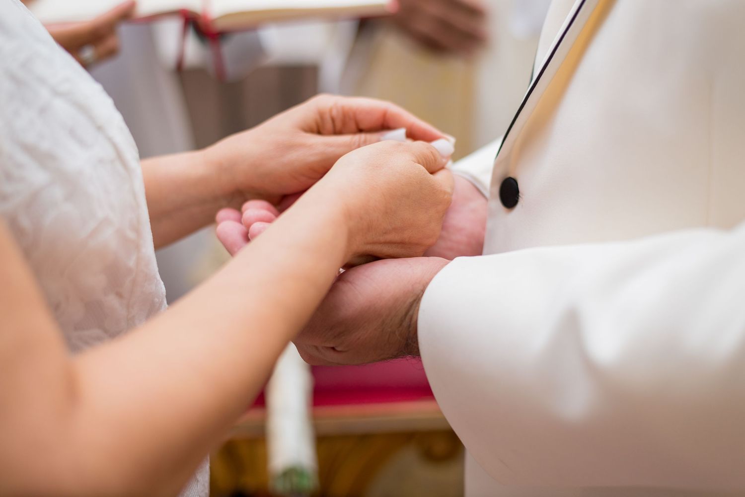 Close-up of priest holding hands of bride and groom during wedding blessing ceremony.