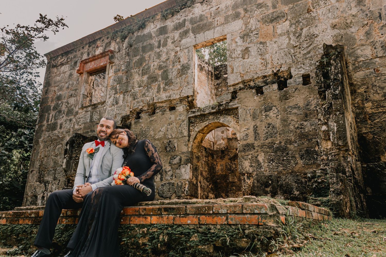 Couple embracing at ancient stone ruins with colorful wedding bouquet outdoors.