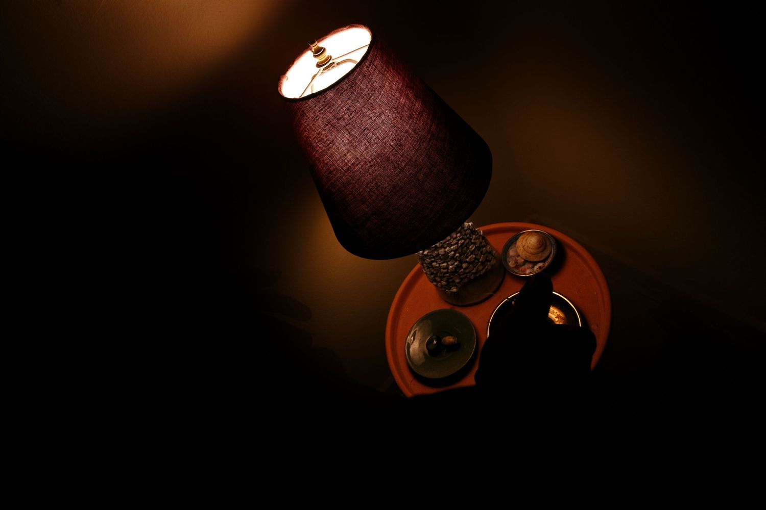 Small decorative lamp glowing warmly on a dark wooden shelf with decorative objects in dim light.
