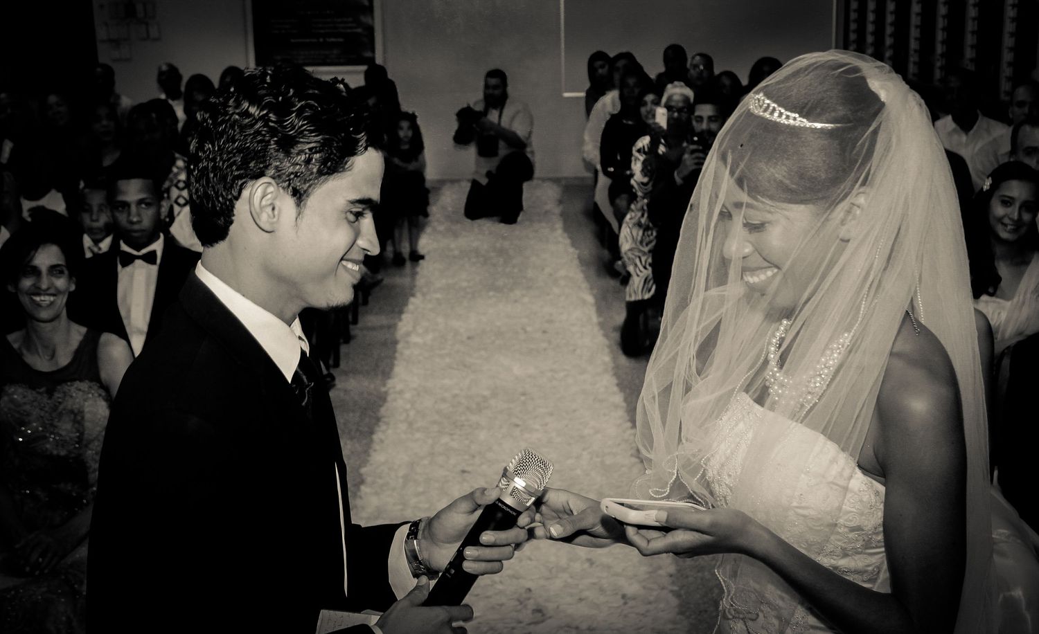Black and white photo of a bride and groom exchanging rings during a wedding ceremony.