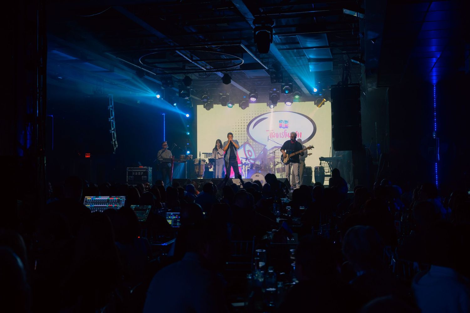 A band performs on a large illuminated stage before a seated audience at a formal indoor corporate event.