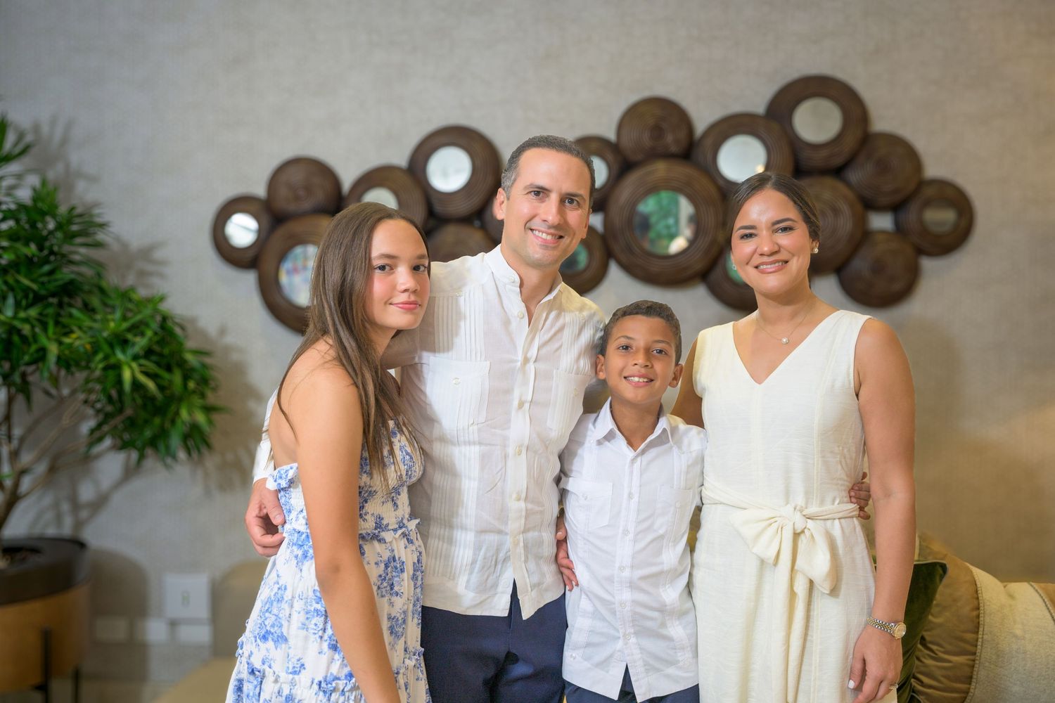 Happy family of four posing together in elegant white outfits at an indoor venue.