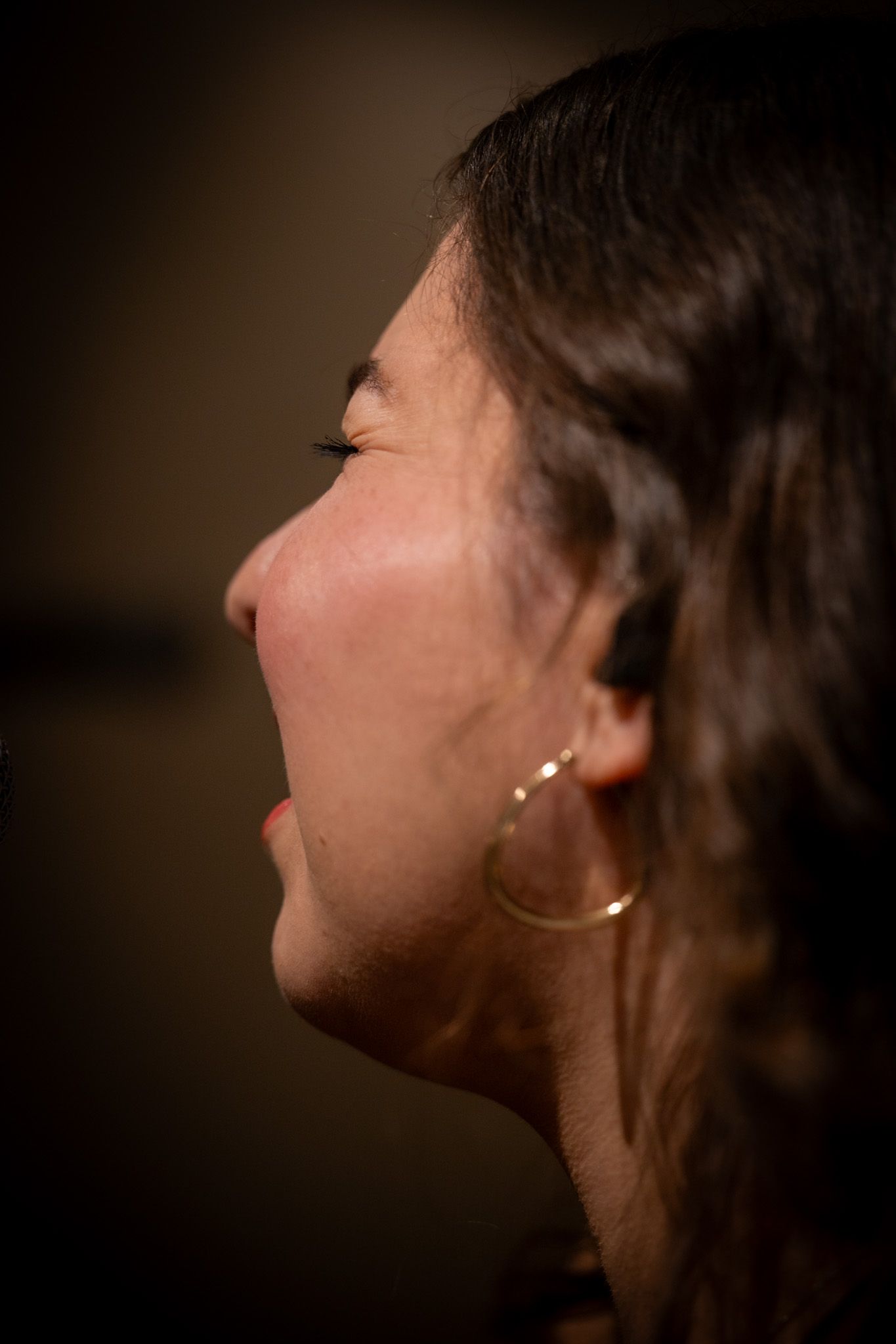 Close-up side profile of a woman with dark hair and gold hoop earring.
