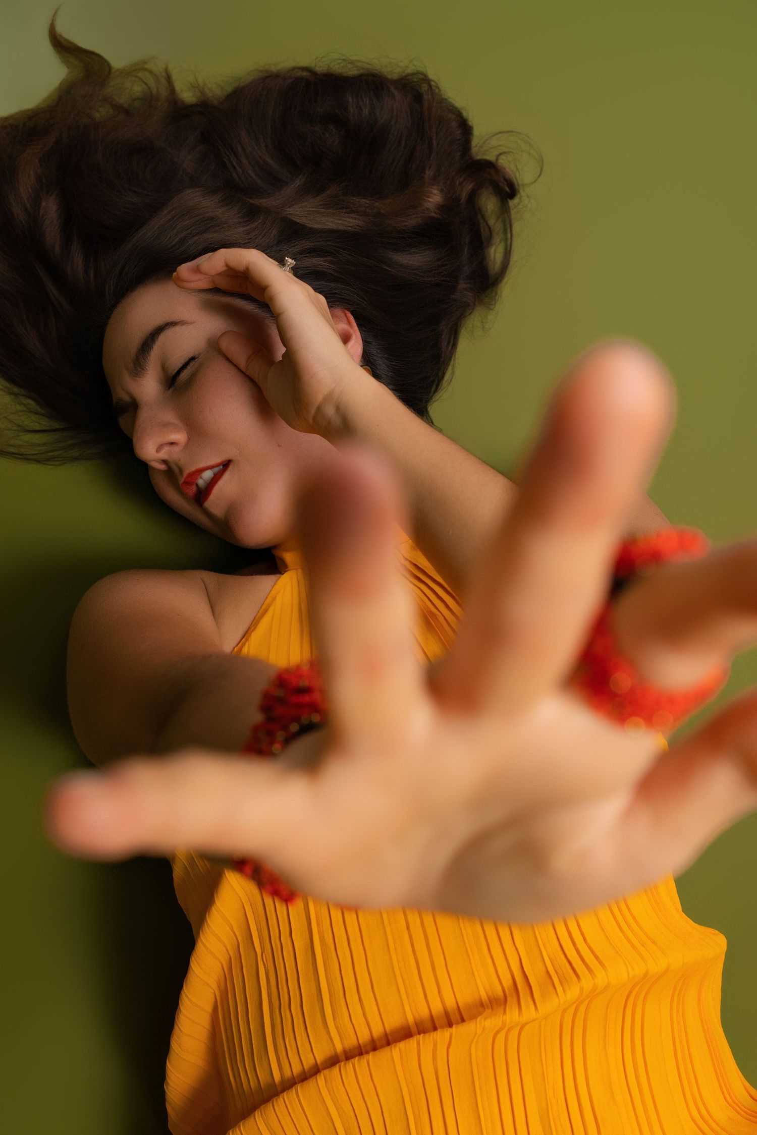Woman in yellow dress lying down reaching toward camera on green background.