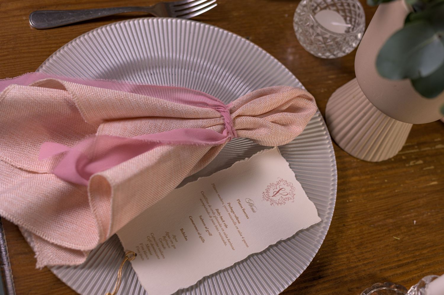 Elegant wedding place setting with pink linen napkin tied with ribbon on striped plate with menu card.