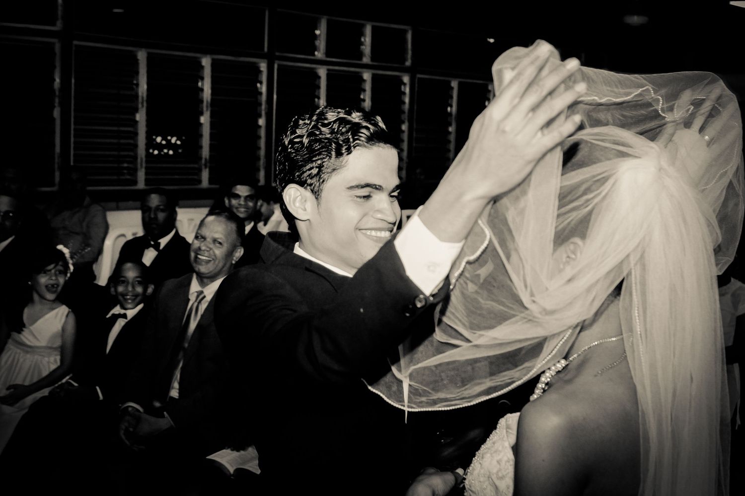Black and white photo of groom lifting brides veil during traditional wedding ceremony.
