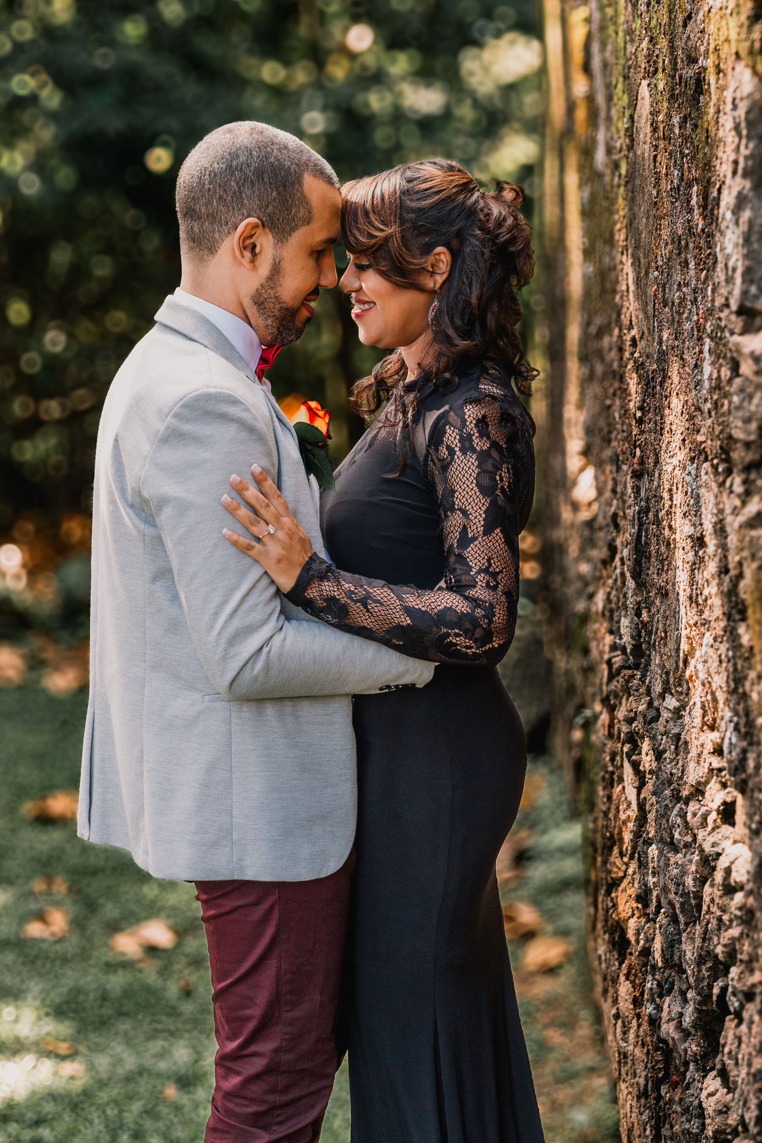 Romantic couple embracing and smiling near tree in lush garden setting.