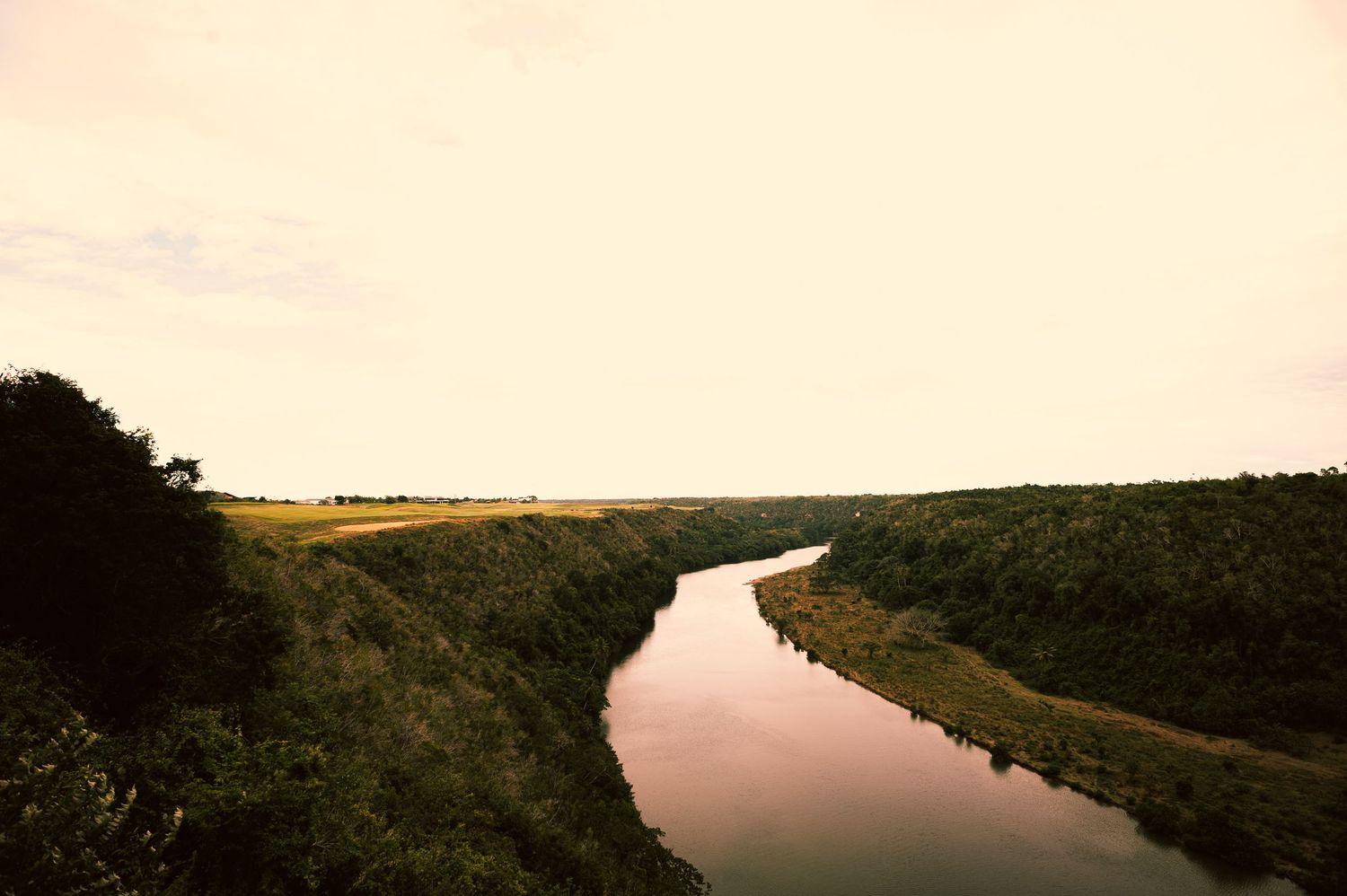 Winding river cutting through lush green landscape at dusk with a pale sky reflecting on calm water.