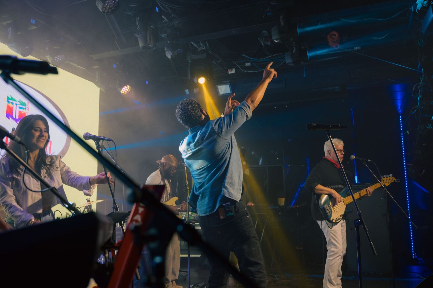 Band performing energetically on stage with colorful lights in a packed concert venue.