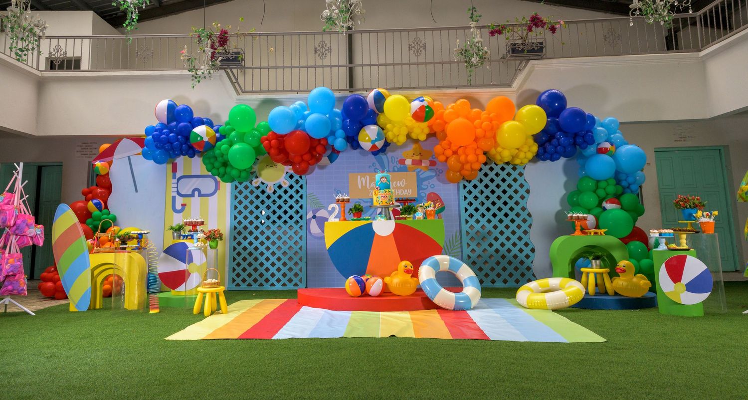 Vibrant pool party birthday decoration with colorful balloon arch and festive themed party setup.
