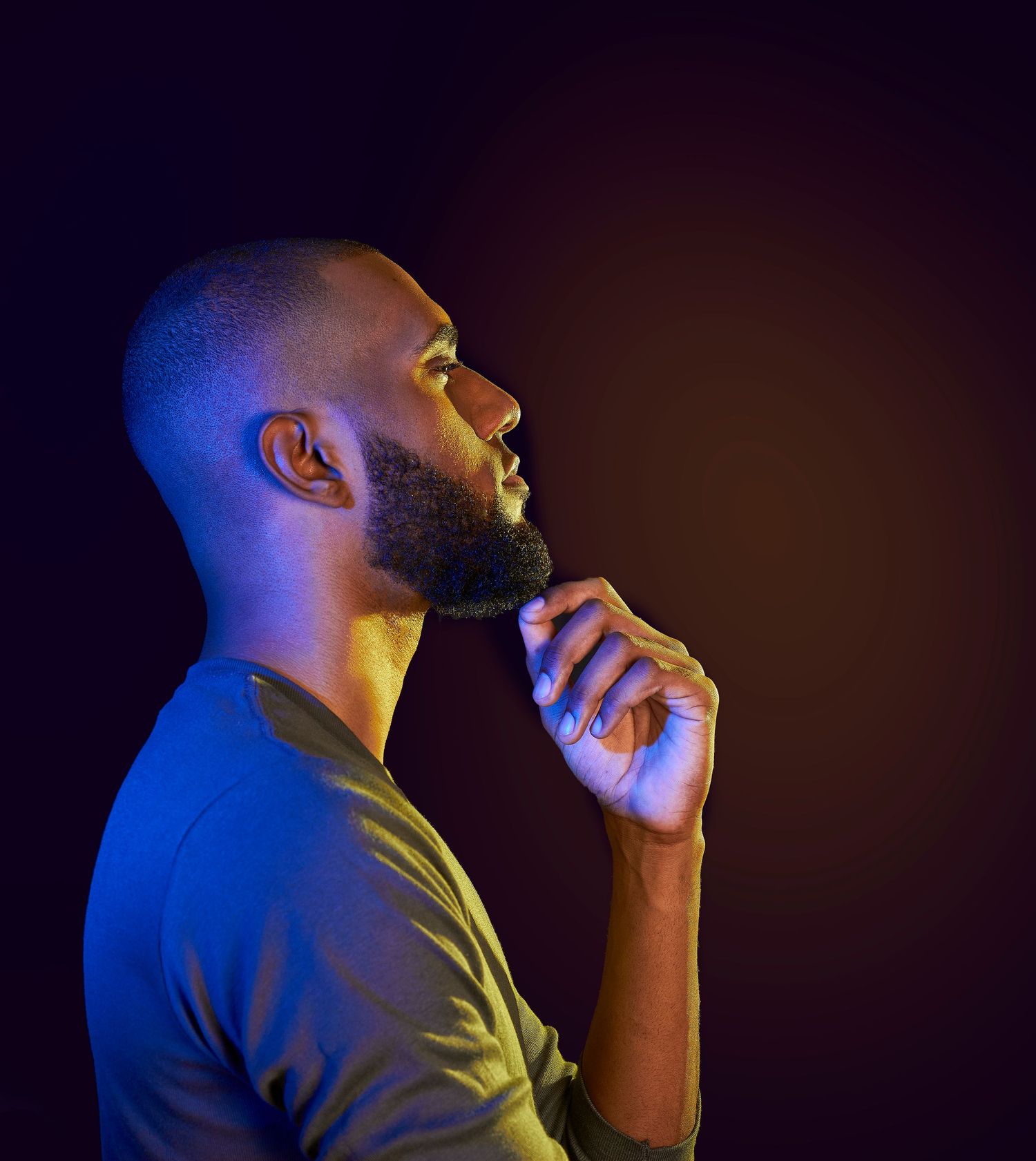 Side profile of bearded Black man in blue and yellow neon lighting looking upward.