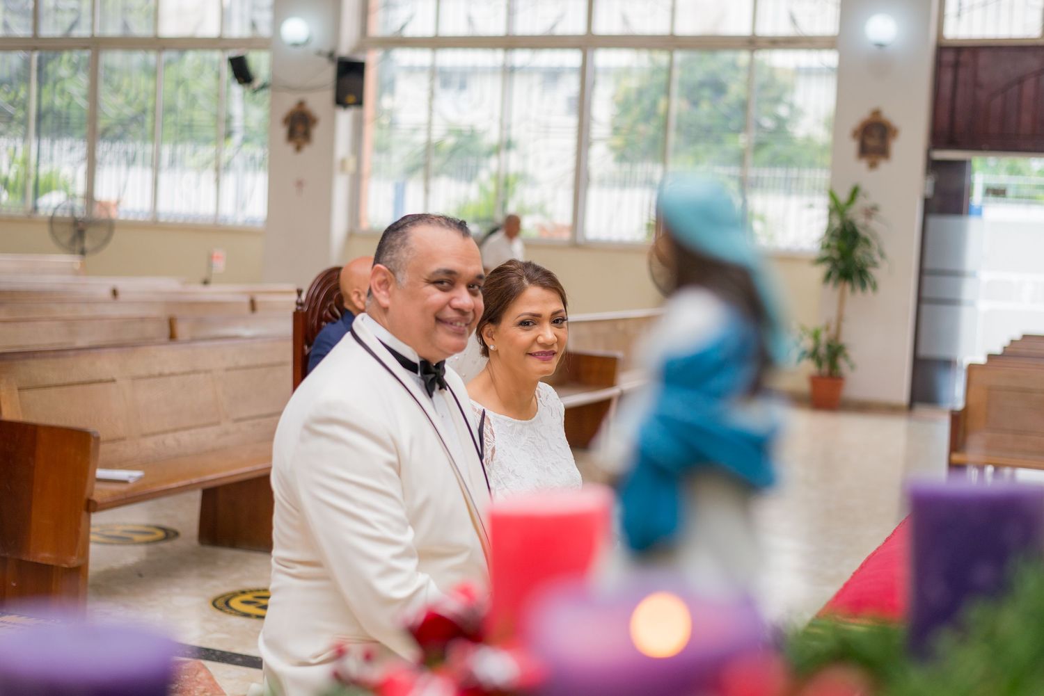 Smiling bride and groom seated in church during their Catholic wedding ceremony.