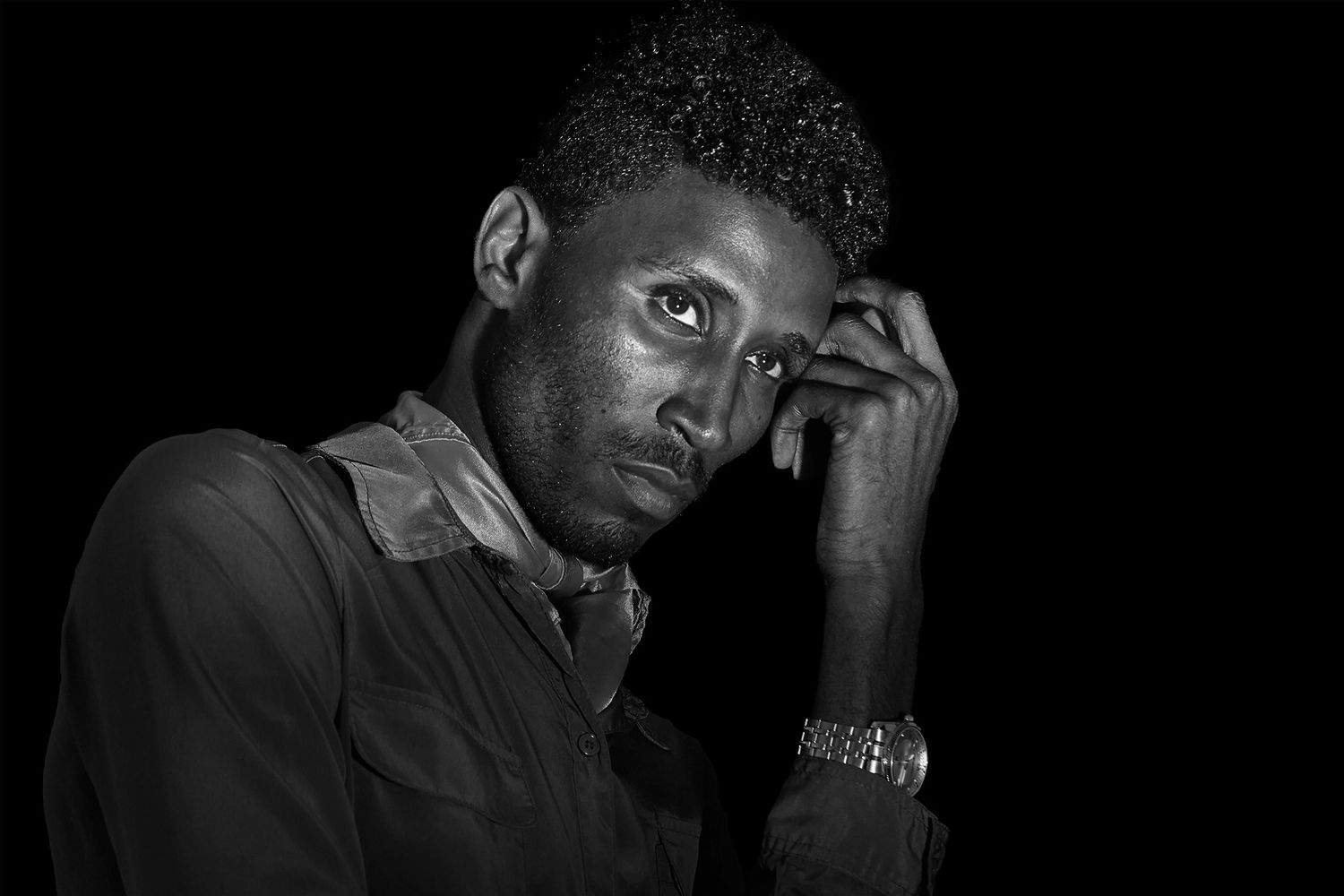 Black and white portrait of a thoughtful young man resting his hand on his temple.