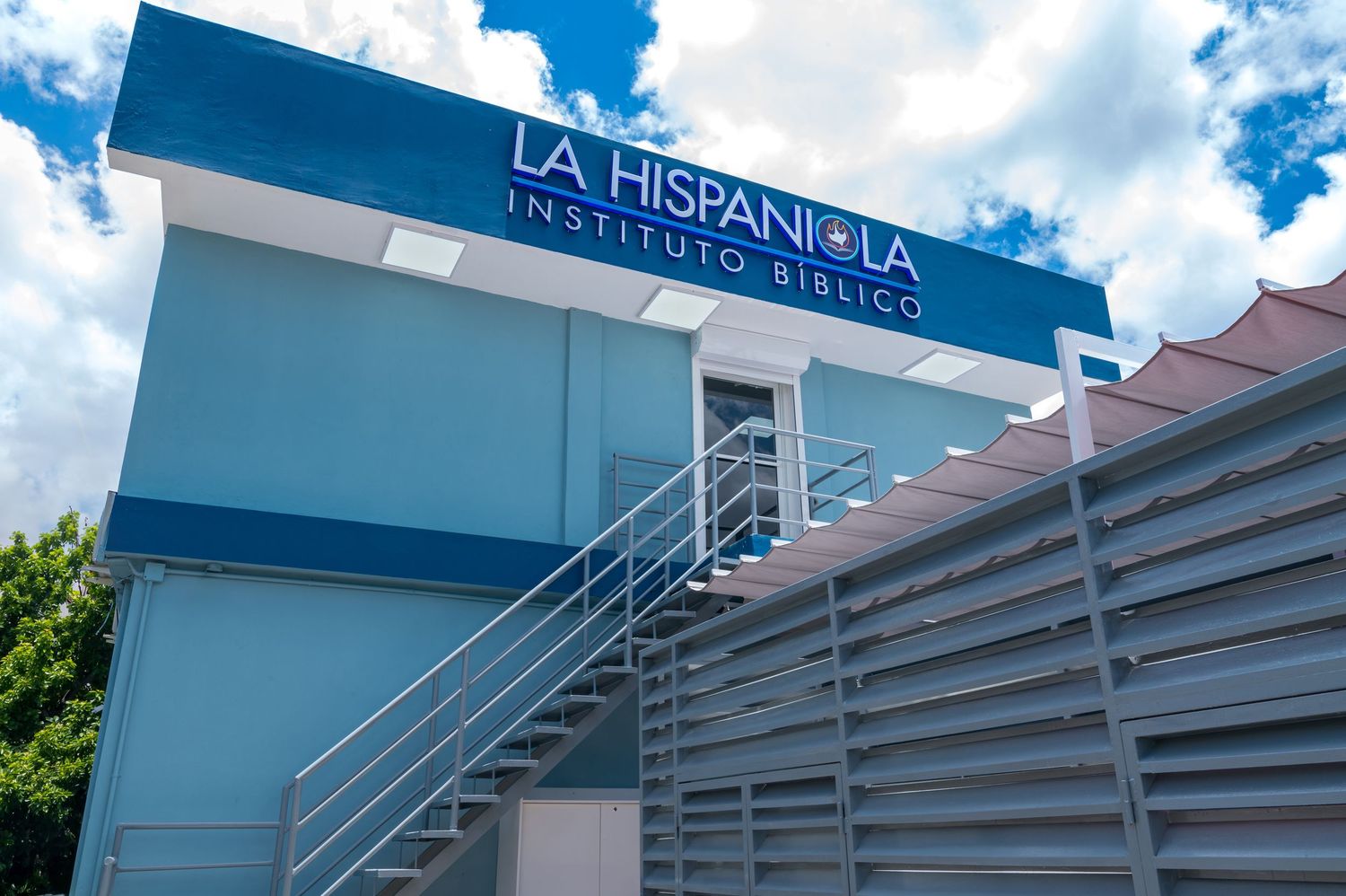 La Hispaniola Instituto Biblico modern blue and white building exterior with staircase under a cloudy sky.