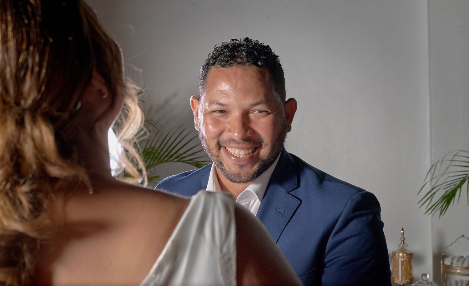 Smiling groom in blue suit gazing at bride during intimate wedding ceremony moment.