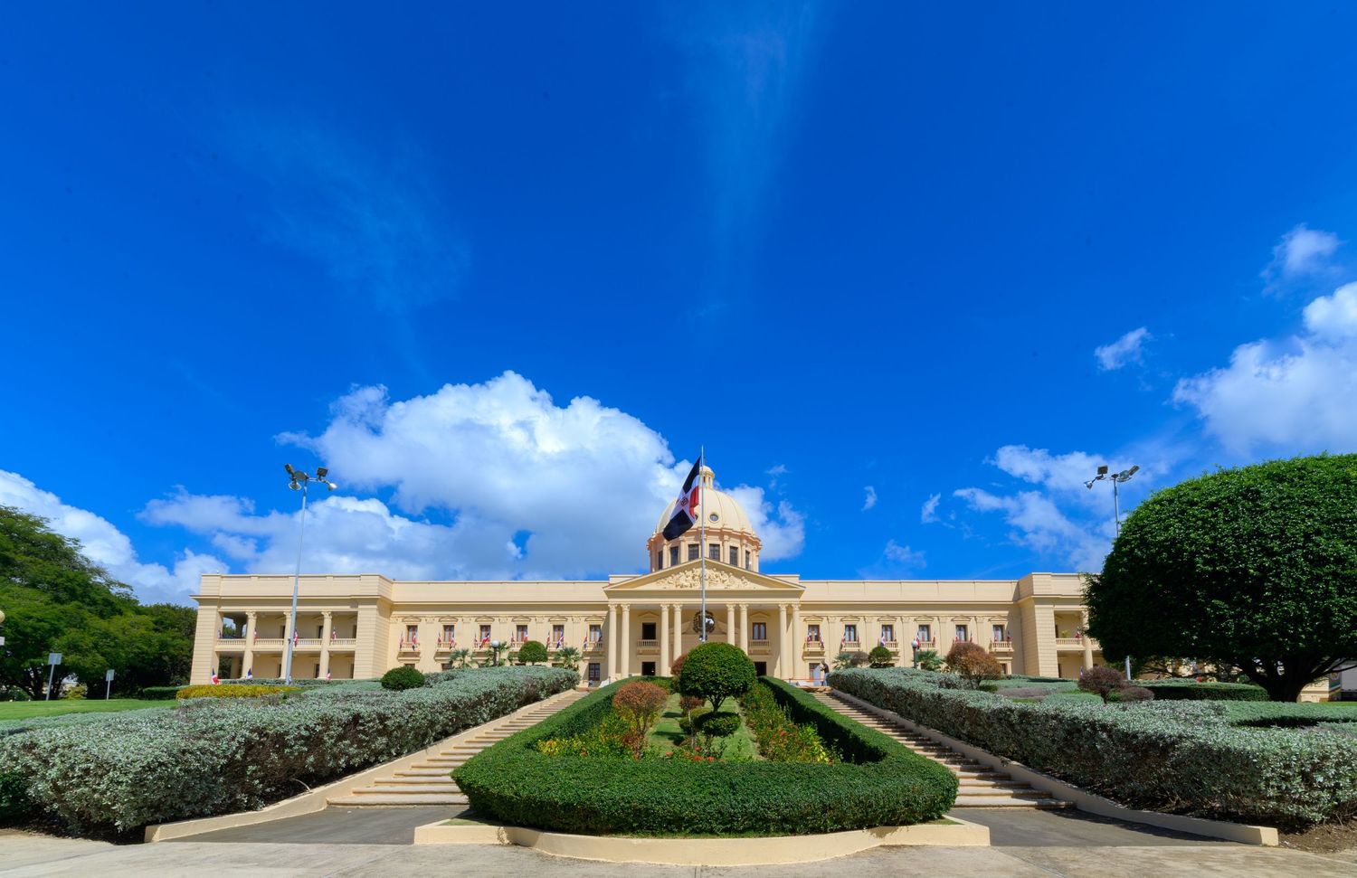 Grand neoclassical government palace with manicured gardens under a vivid blue sky in Santo Domingo, Dominican Republic.