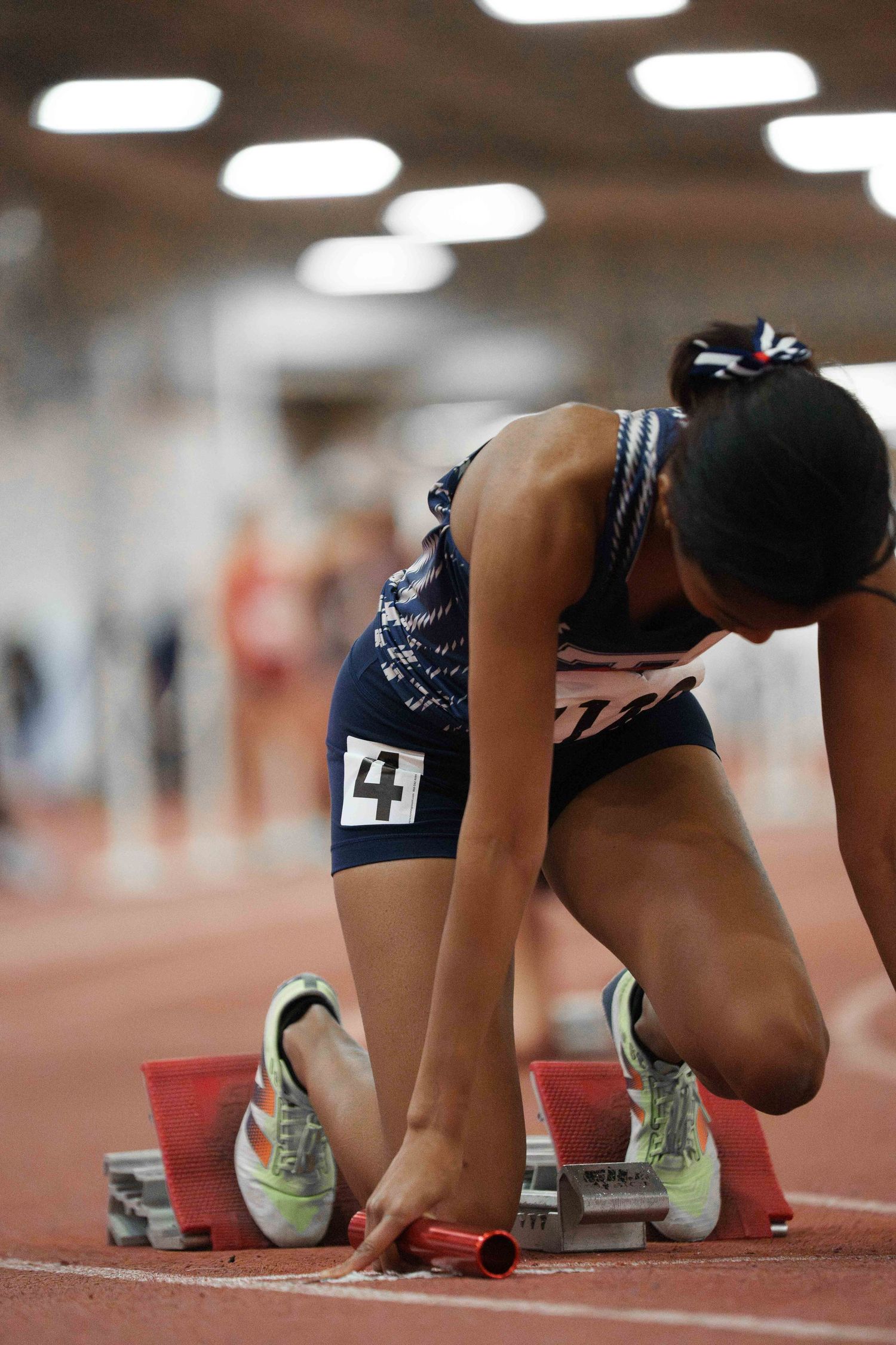 A young female track runner in the starting block position on the track.