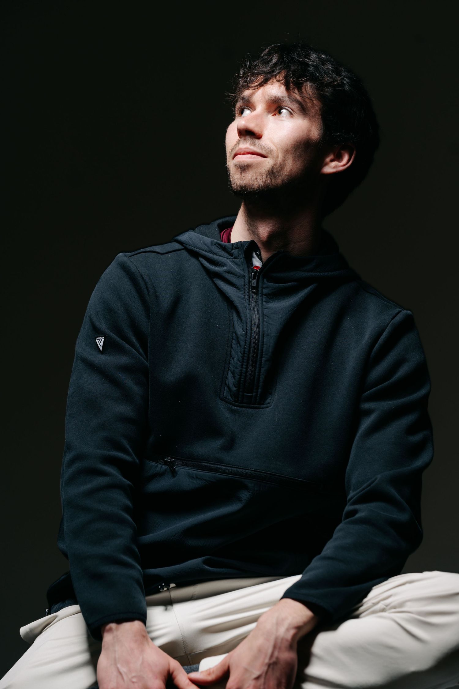Flash studio portrait of a young white man in front of a dark background. He looks up to the left toward the light looking curious.