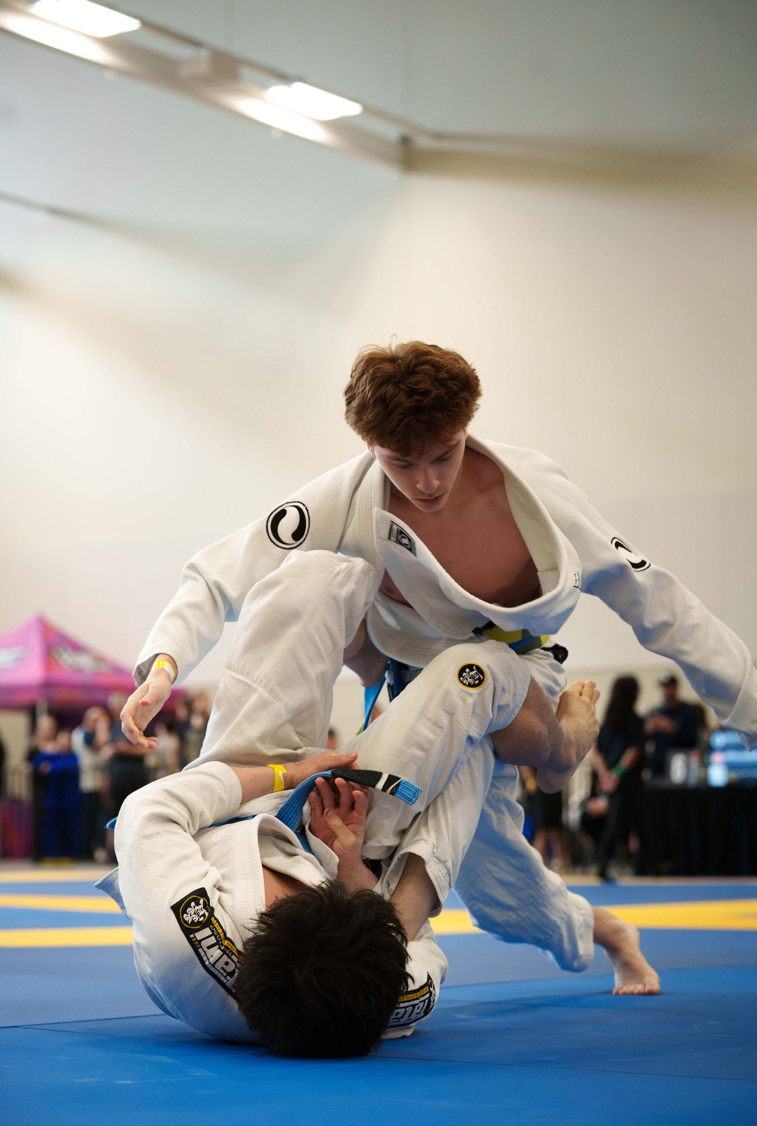 Two young male BJJ fighters wearing white gis grapple on the ground.